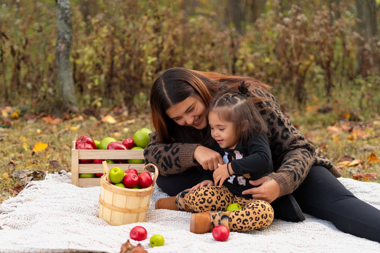 Family enjoying a fall picnic with red apples on a white blanket outdoors.