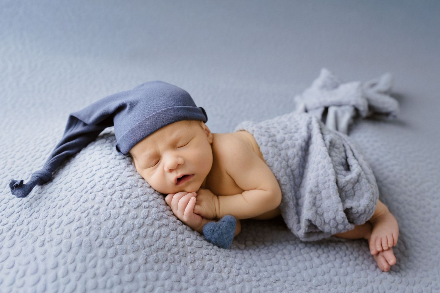 Sleeping newborn baby wearing a blue knit slouchy hat, wrapped in a soft gray blanket during in-home newborn session North Central IN