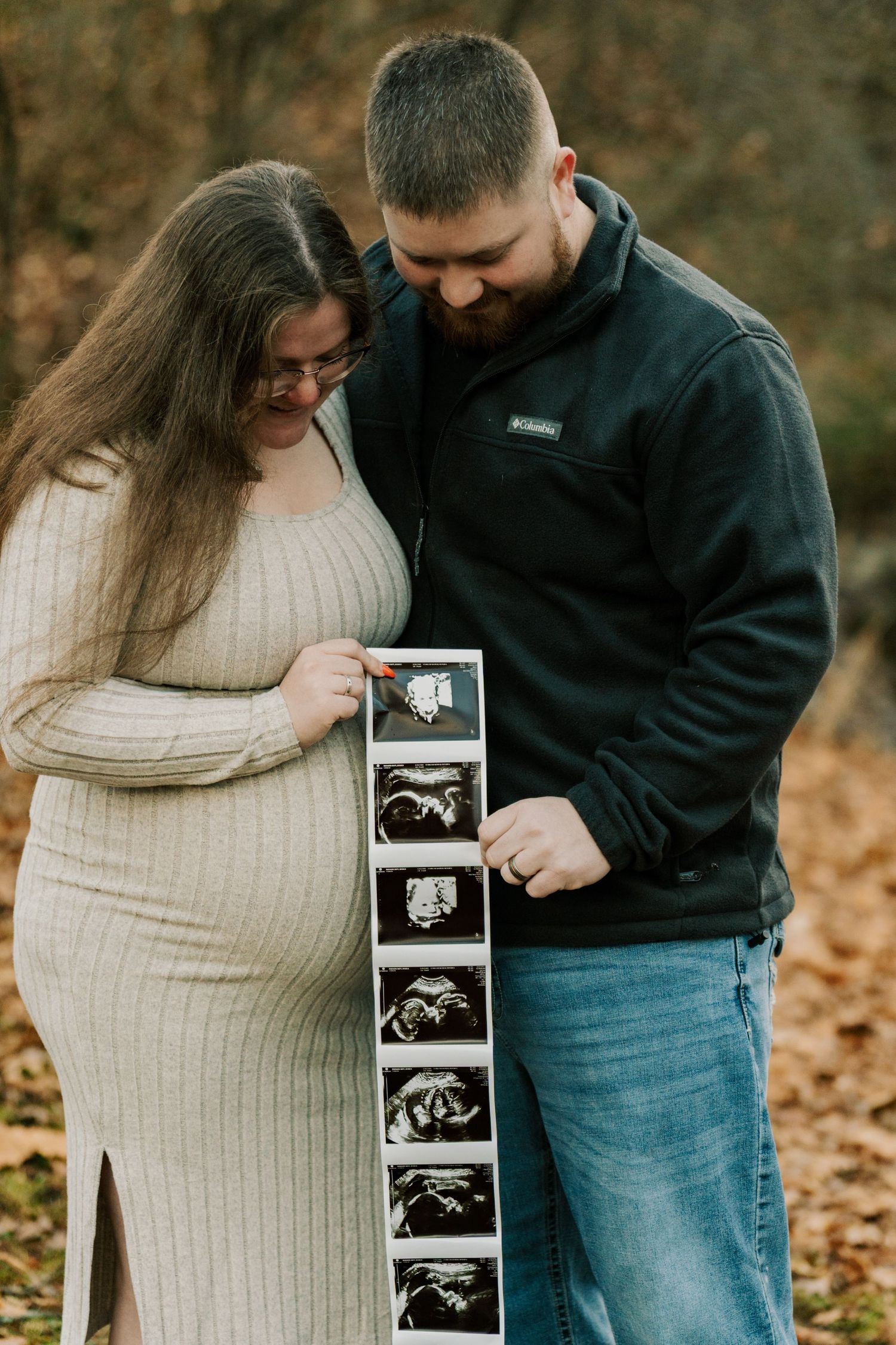 Couple sharing ultrasound photos during outdoor pregnancy announcement photoshoot.