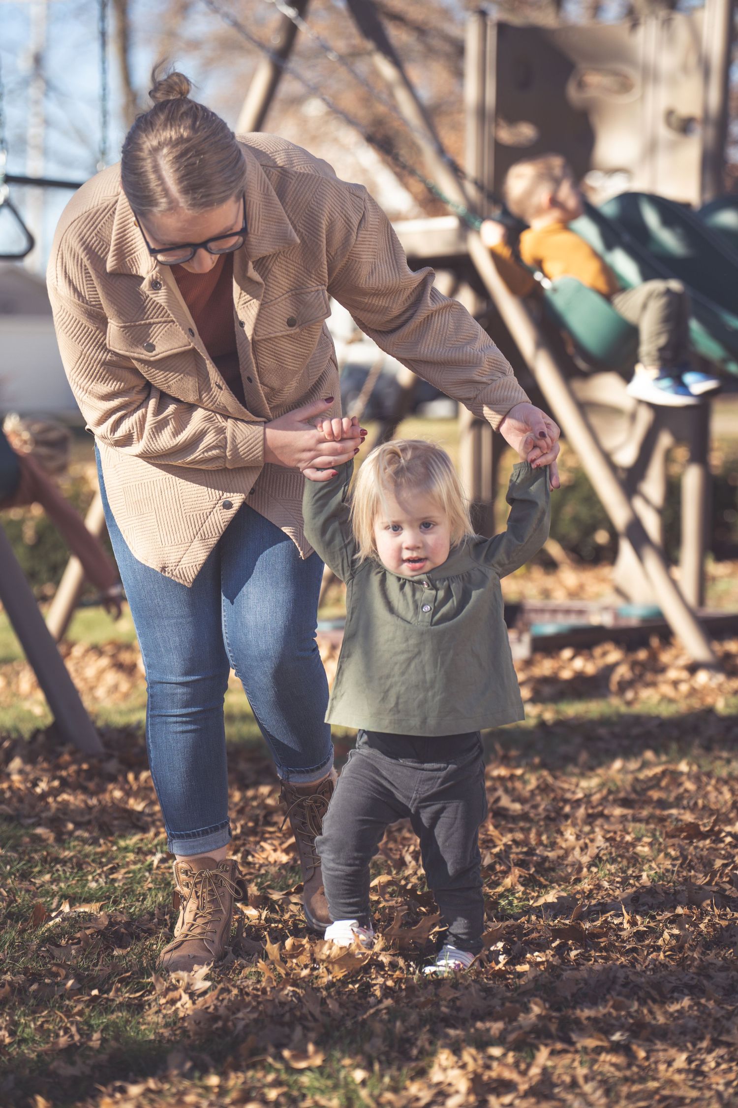 Parent and small child explore fallen autumn leaves together in a wooded outdoor setting.