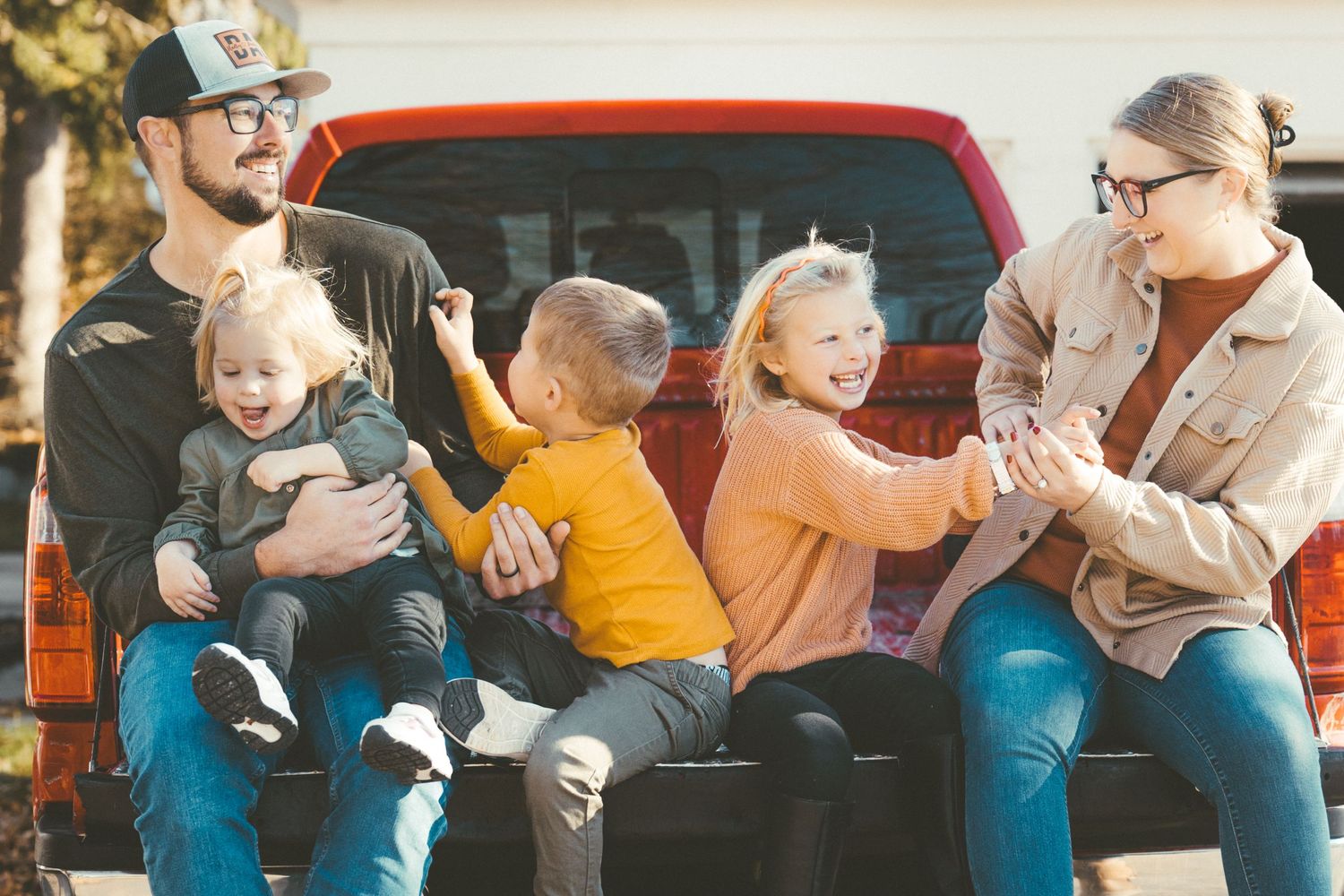 Group enjoying playful moments together on back of red pickup truck.