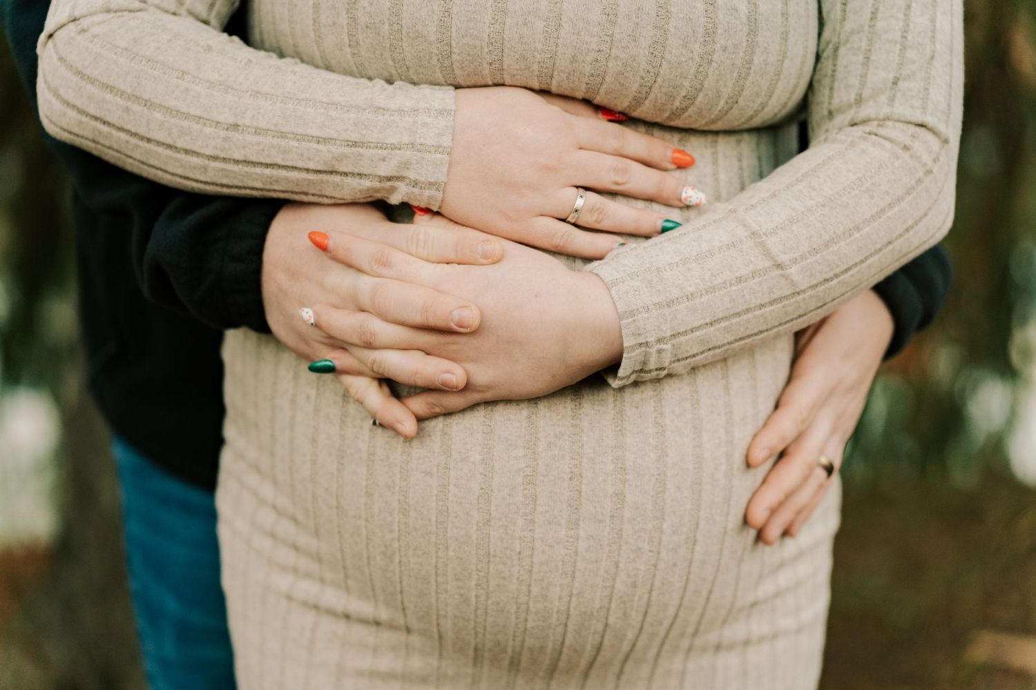 Close-up shot of hands gently resting on a beige ribbed sweater in natural lighting.