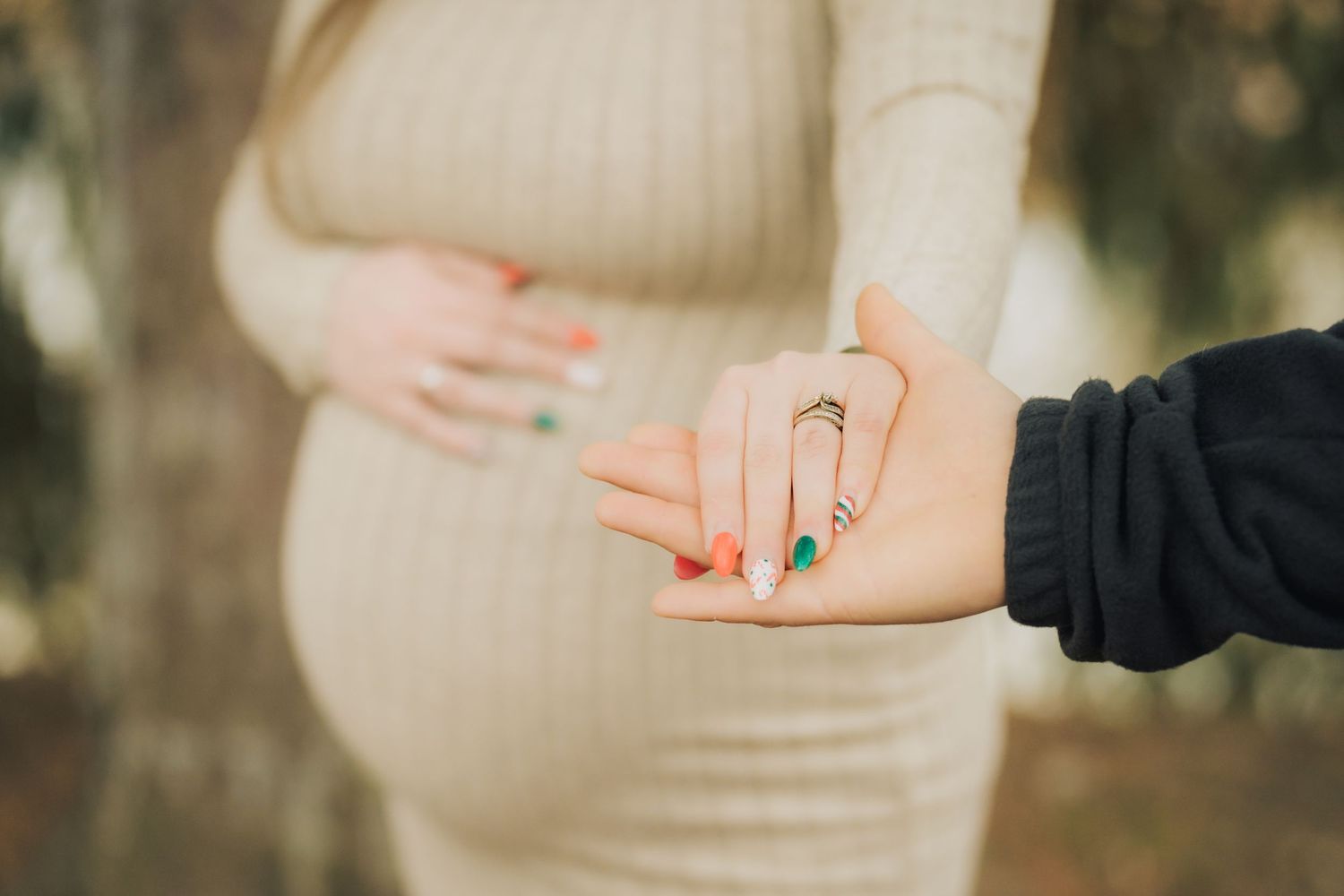 Close up of two hands reaching toward each other against a blurred outdoor background.