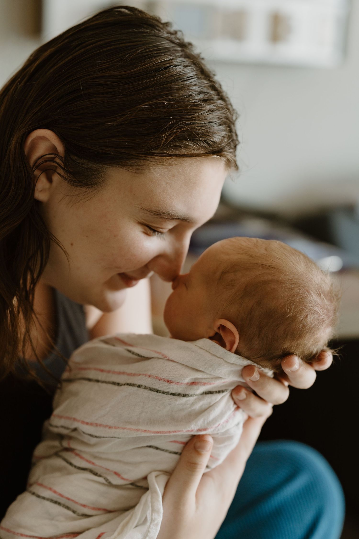 A young mother tenderly touching noses with her swaddled newborn baby during Fresh 48 session in North Central Indiana.