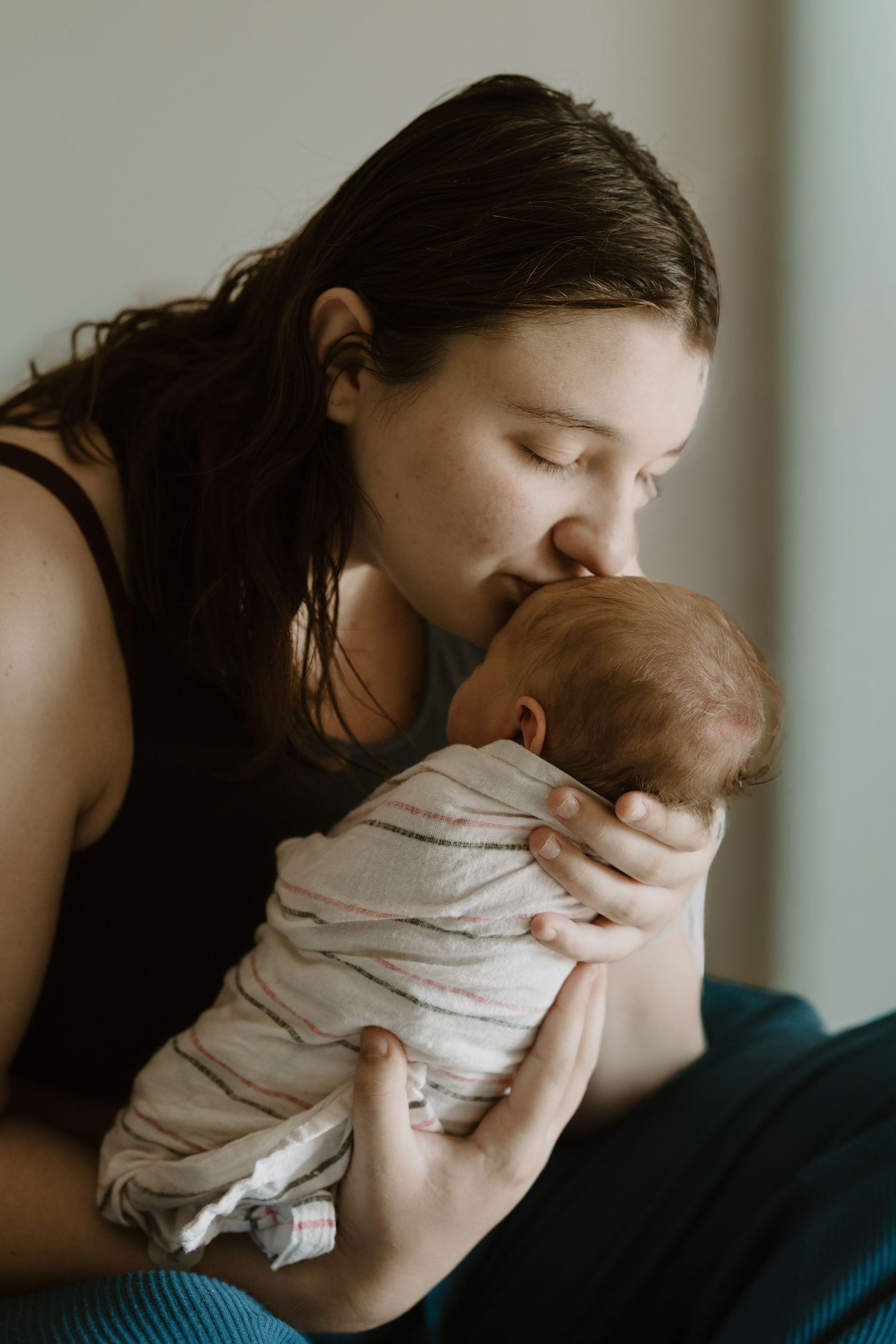 A young mother gently kisses her swaddled newborn baby, sharing a tender moment of love and bonding during Fresh 48 session Miami County, IN