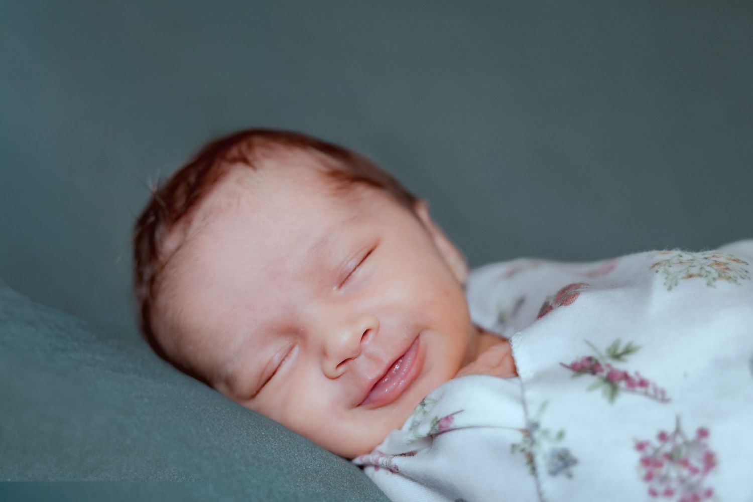 A sleeping baby lies peacefully on white bedding with floral patterns.