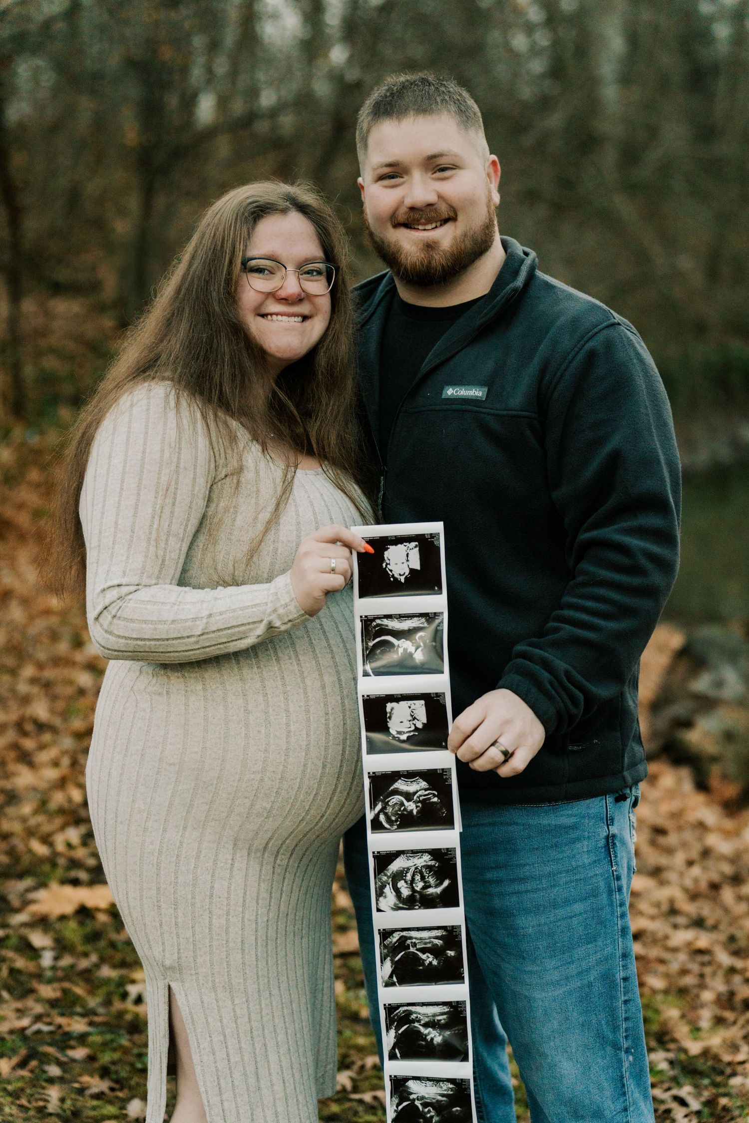 Happy couple displaying ultrasound images during autumn maternity photo session.