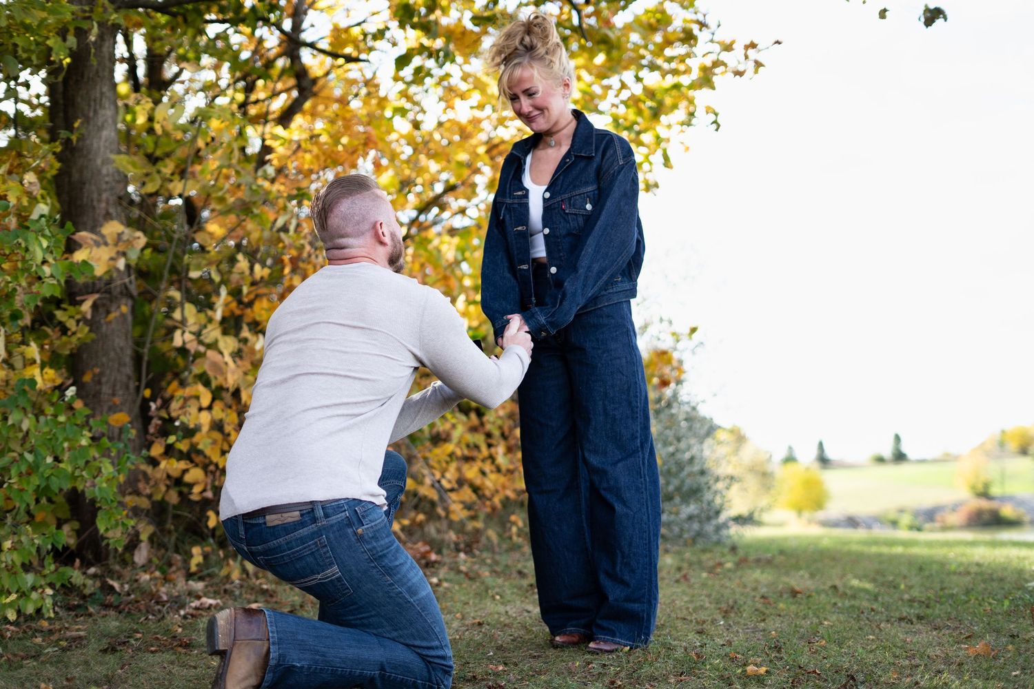 Couple in casual attire sharing playful moments in an autumn outdoor setting with yellow leaves.