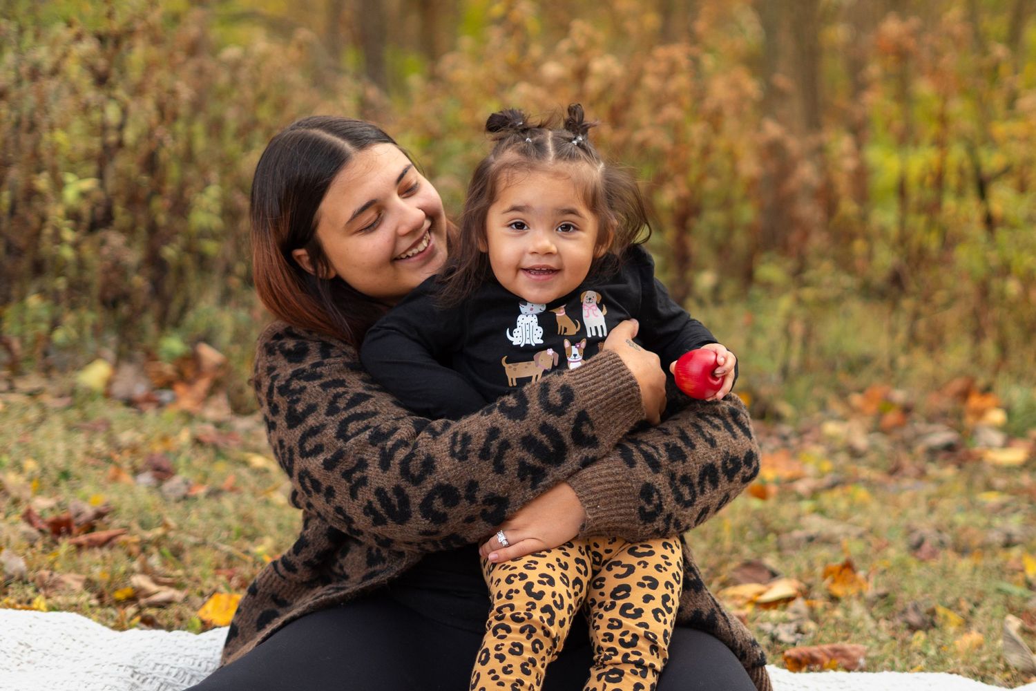 Sweet autumn family moment with leopard print and black outfits among fallen leaves.