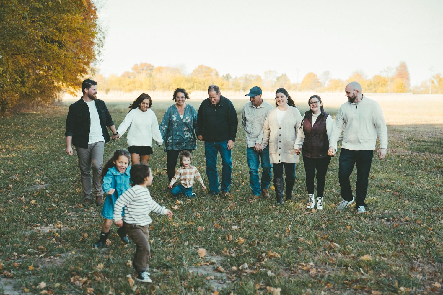 Extended family members lined up for a panoramic photo in a fall field.