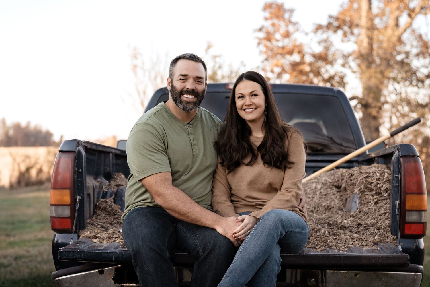 Casual outdoor portrait session with couple sitting on the back of a red pickup truck.