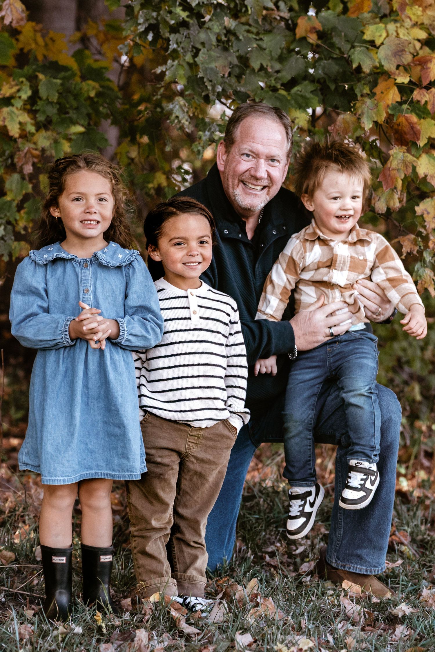 Row of children sitting together on a log showing playful expressions during fall.