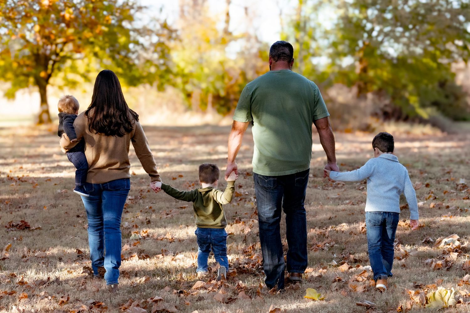 Back view of family walking together through fallen leaves in autumn.