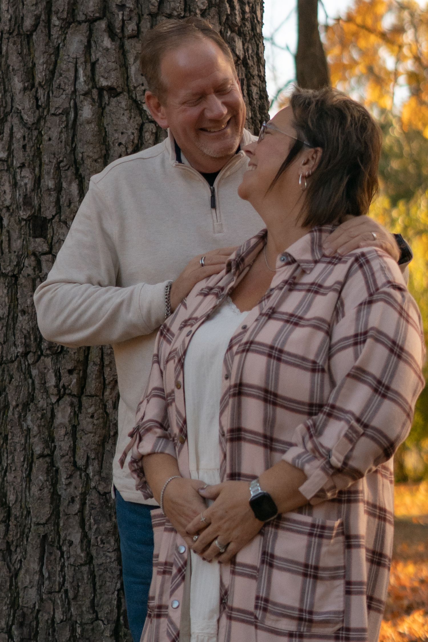 A couple shares an intimate moment against a tree trunk surrounded by fall colors.