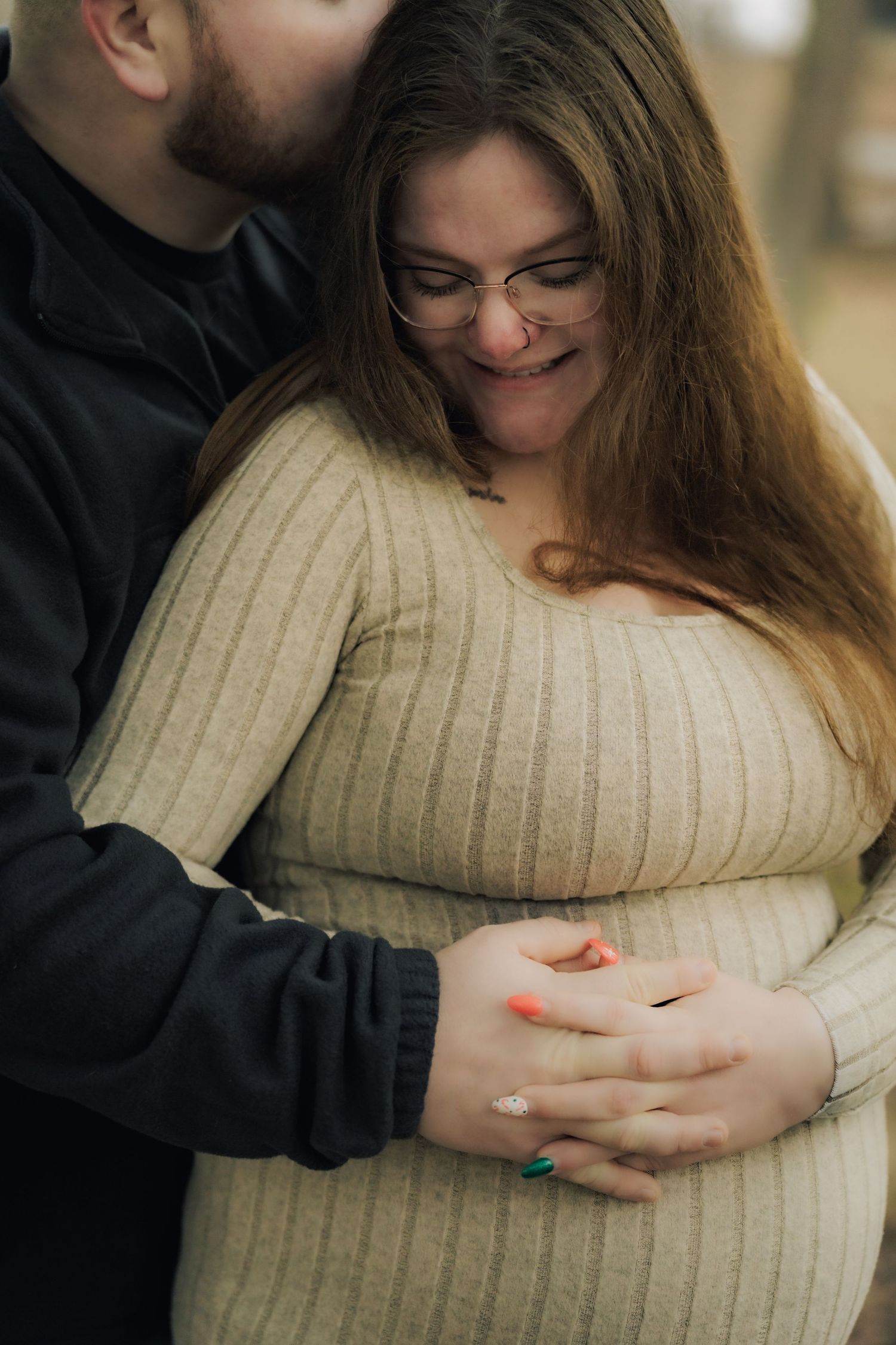 Intimate moment captured showing hands embracing a beige sweater against a blurred outdoor background.