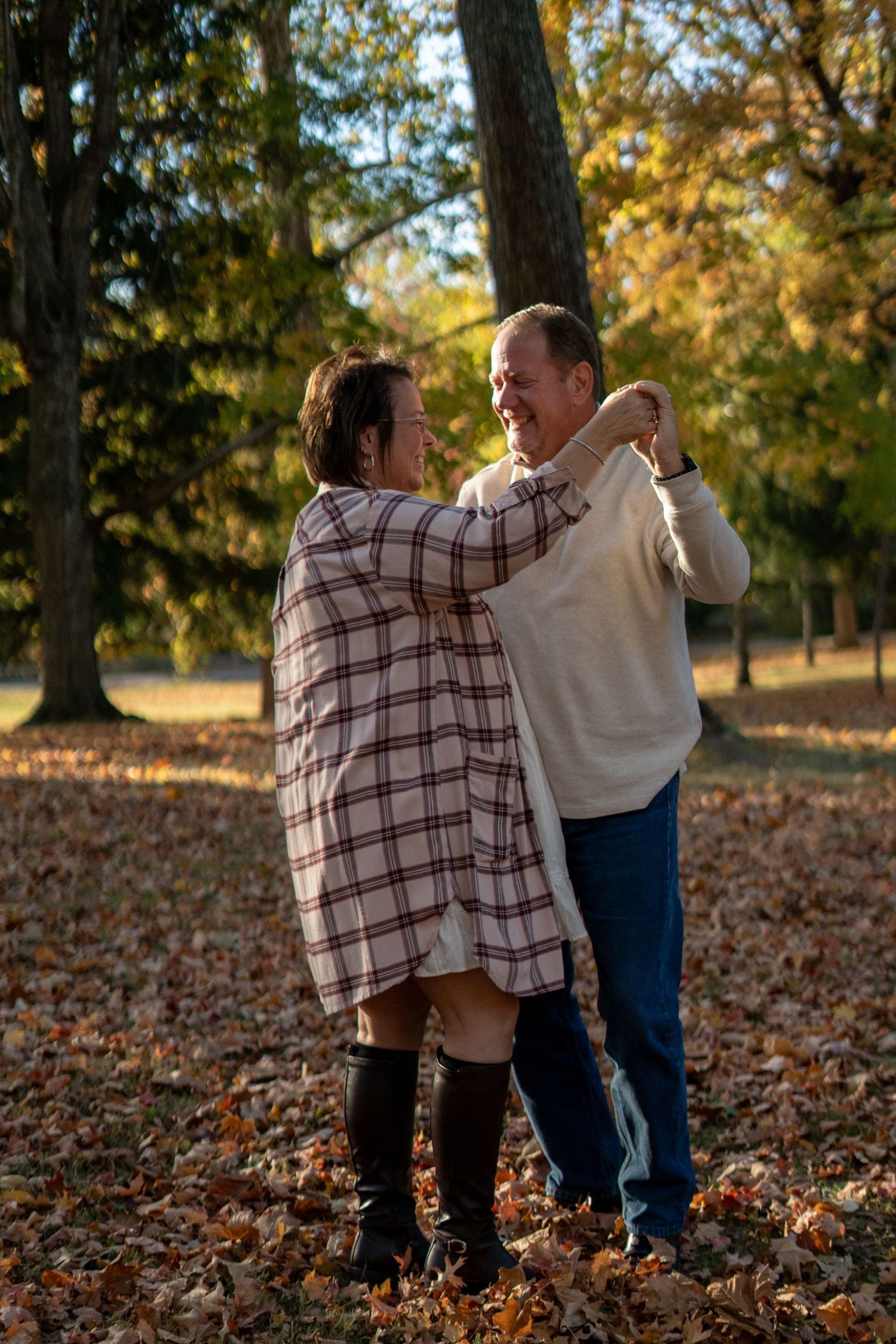 Two people dance playfully together in a park filled with autumn leaves.