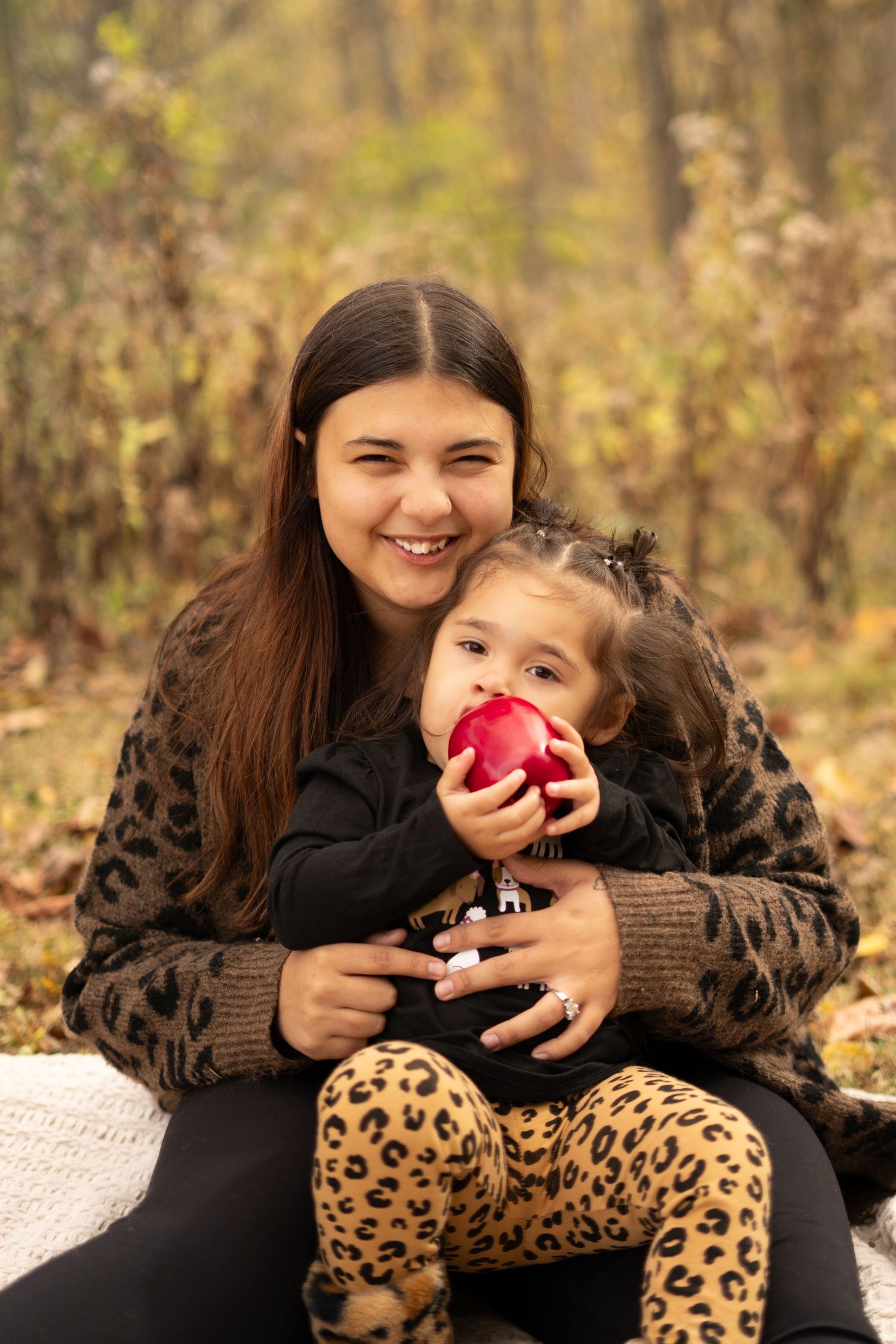 Mother and child sharing red apples during fall photoshoot with leopard print details.