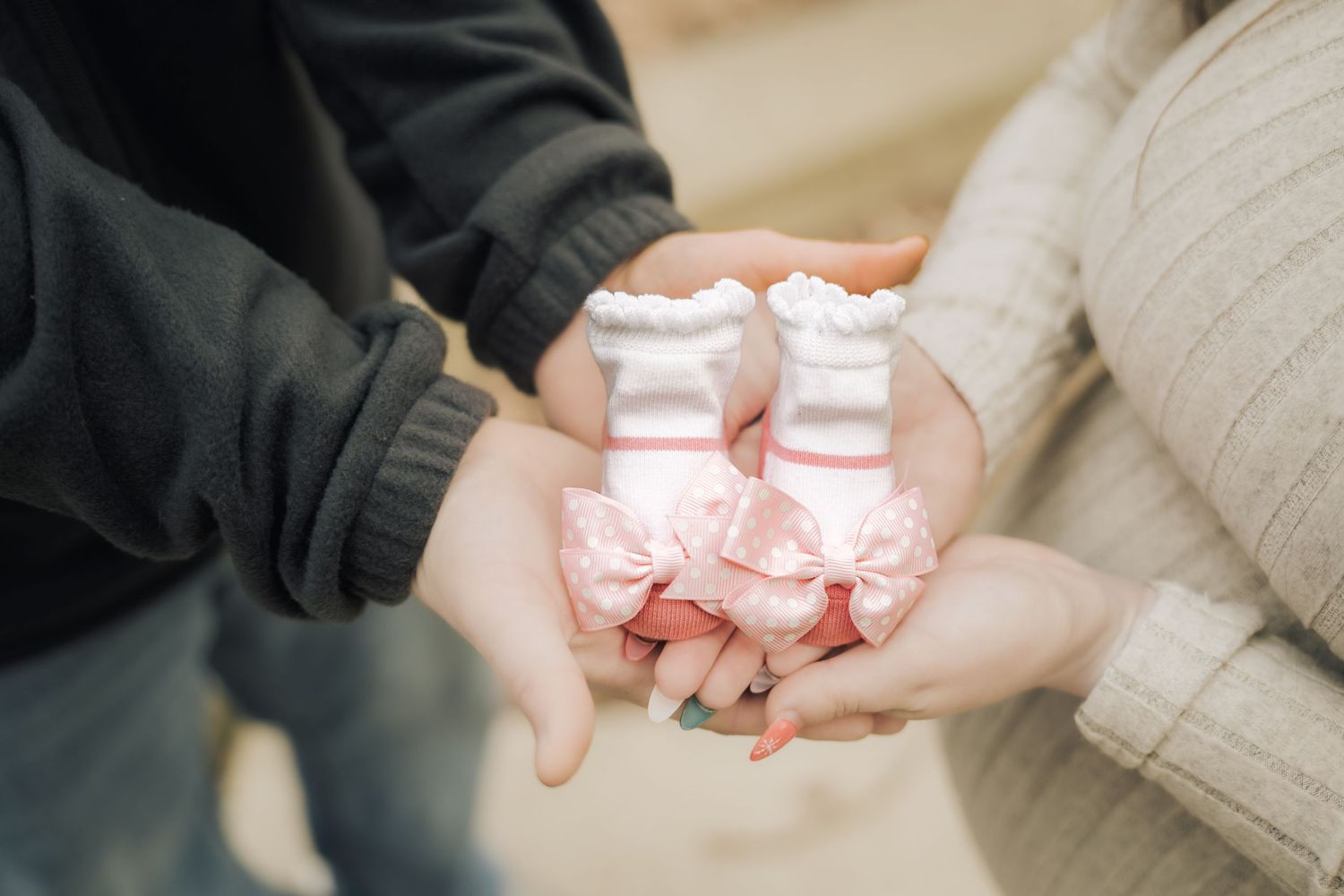Hands holding small pink baby shoes against a soft beige background.
