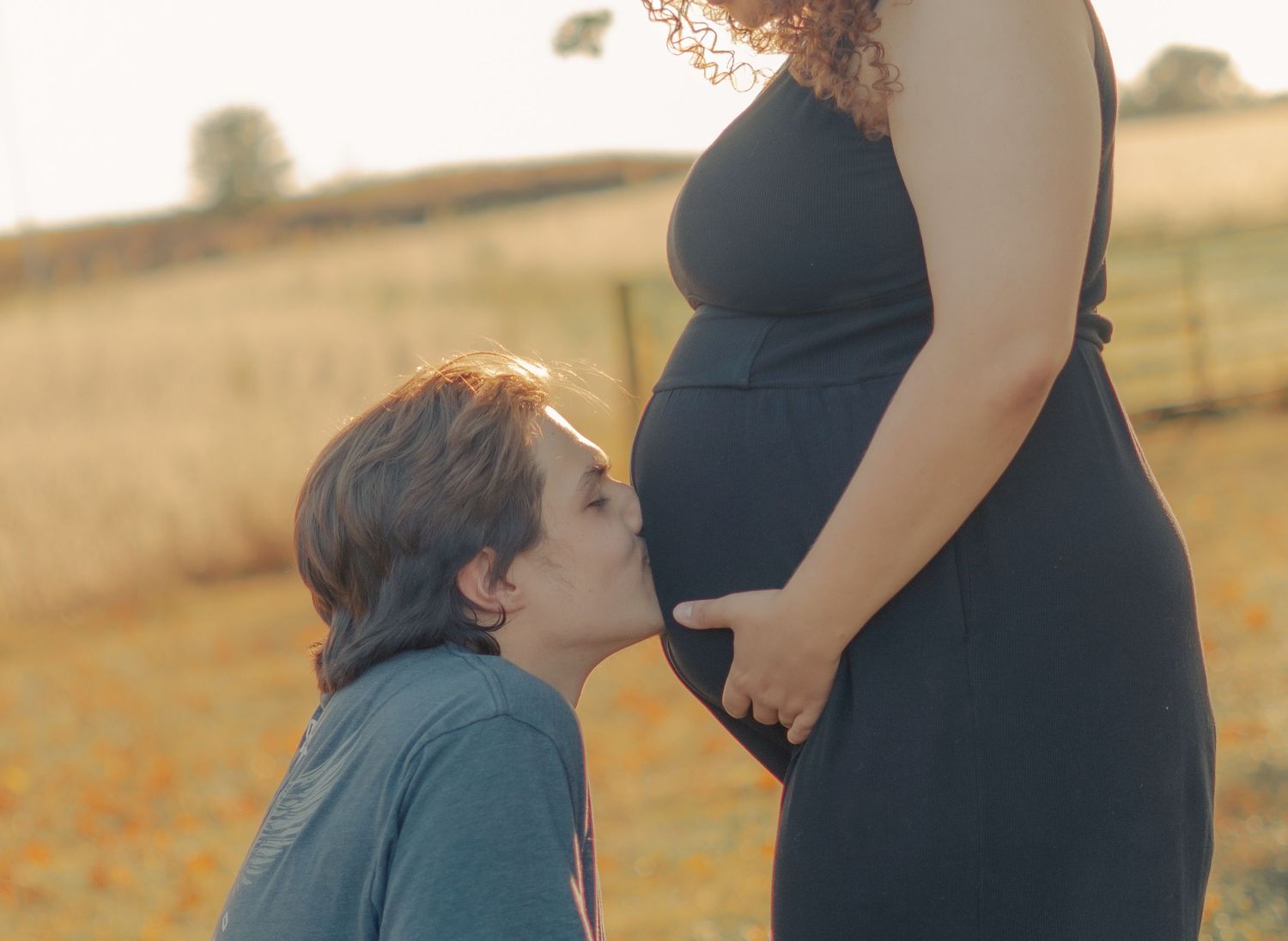A tender maternity moment captured in golden sunlight against a rural landscape.