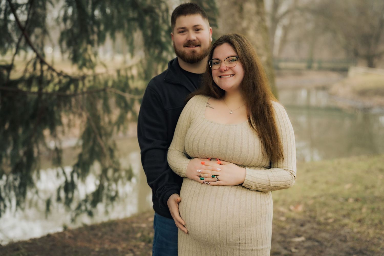 Couple embracing in casual outfits during an outdoor autumn photo session by a lake.