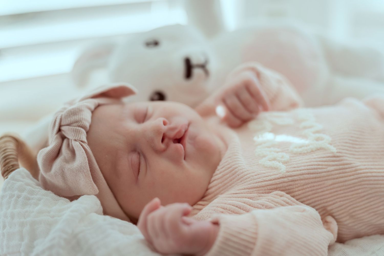 A sleeping infant rests peacefully on soft white bedding while wearing a cozy beige sweater.