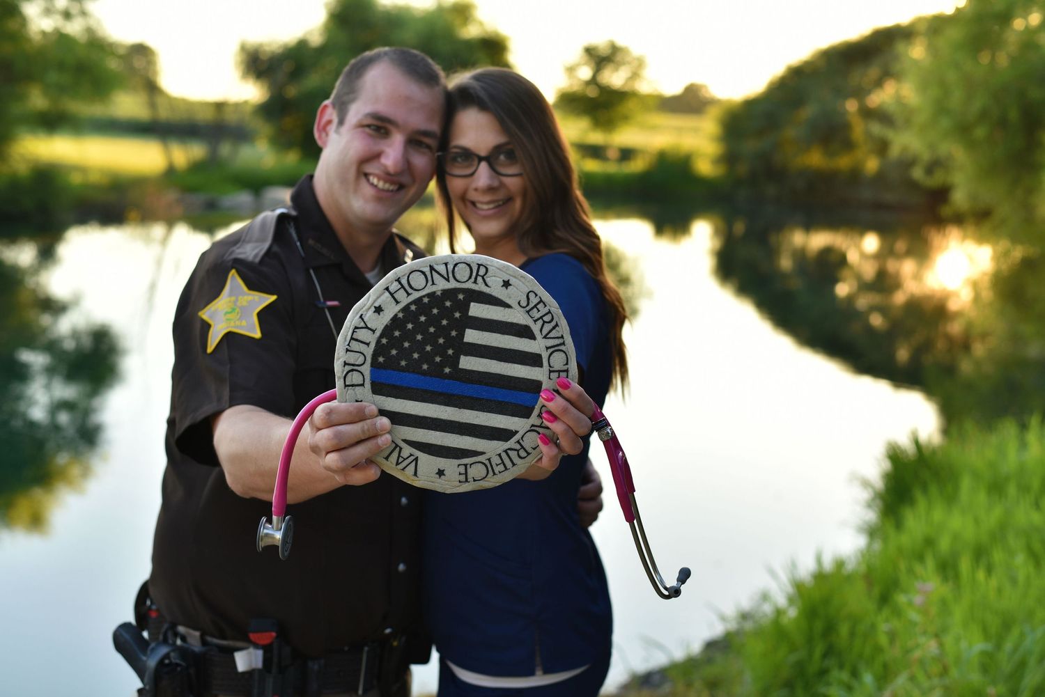 Couple holding American flag themed decor by a lake during golden hour.