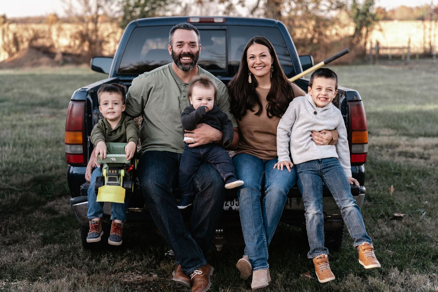 Family sitting together on the tailgate of a pickup truck during an outdoor autumn photoshoot.