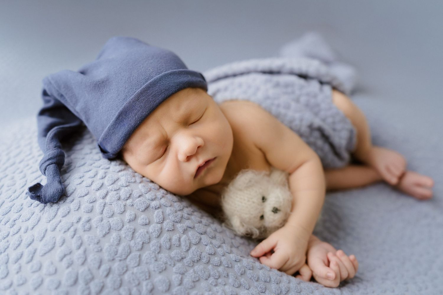 Posed newborn cuddling little bear with sleepy cap during in-home newborn session North Central IN with Bushel & a Peck Photography