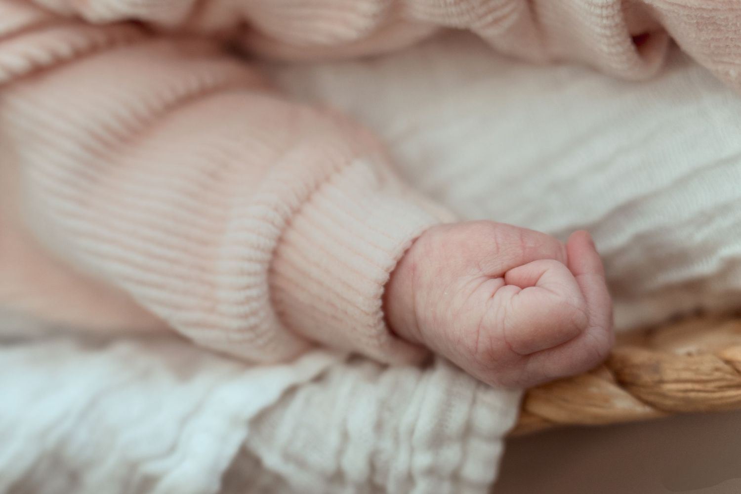 Close-up of a tiny baby hand wearing a soft pink knit sleeve against white bedding.