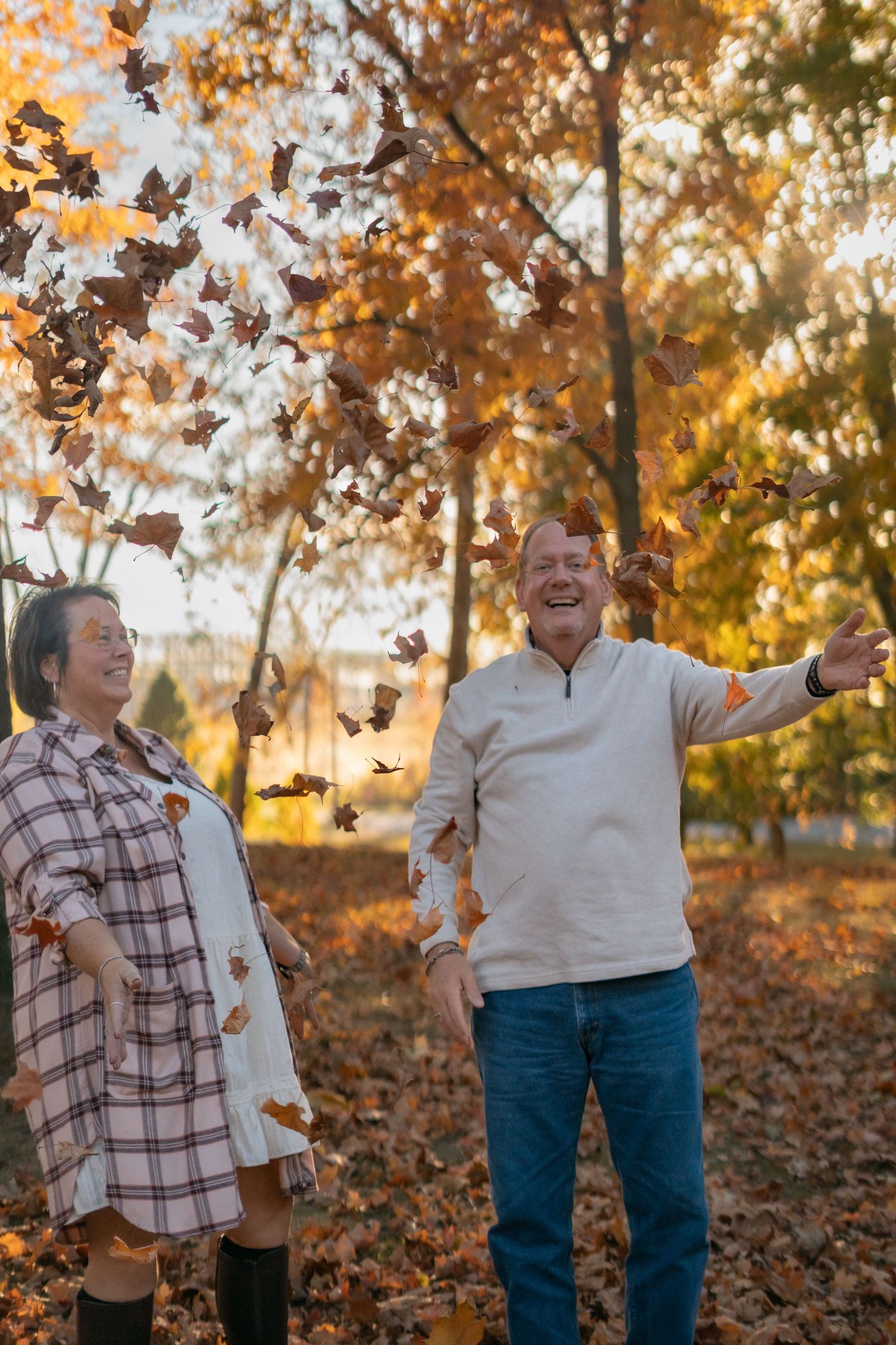 A couple throws autumn leaves in the air during a playful outdoor photoshoot.