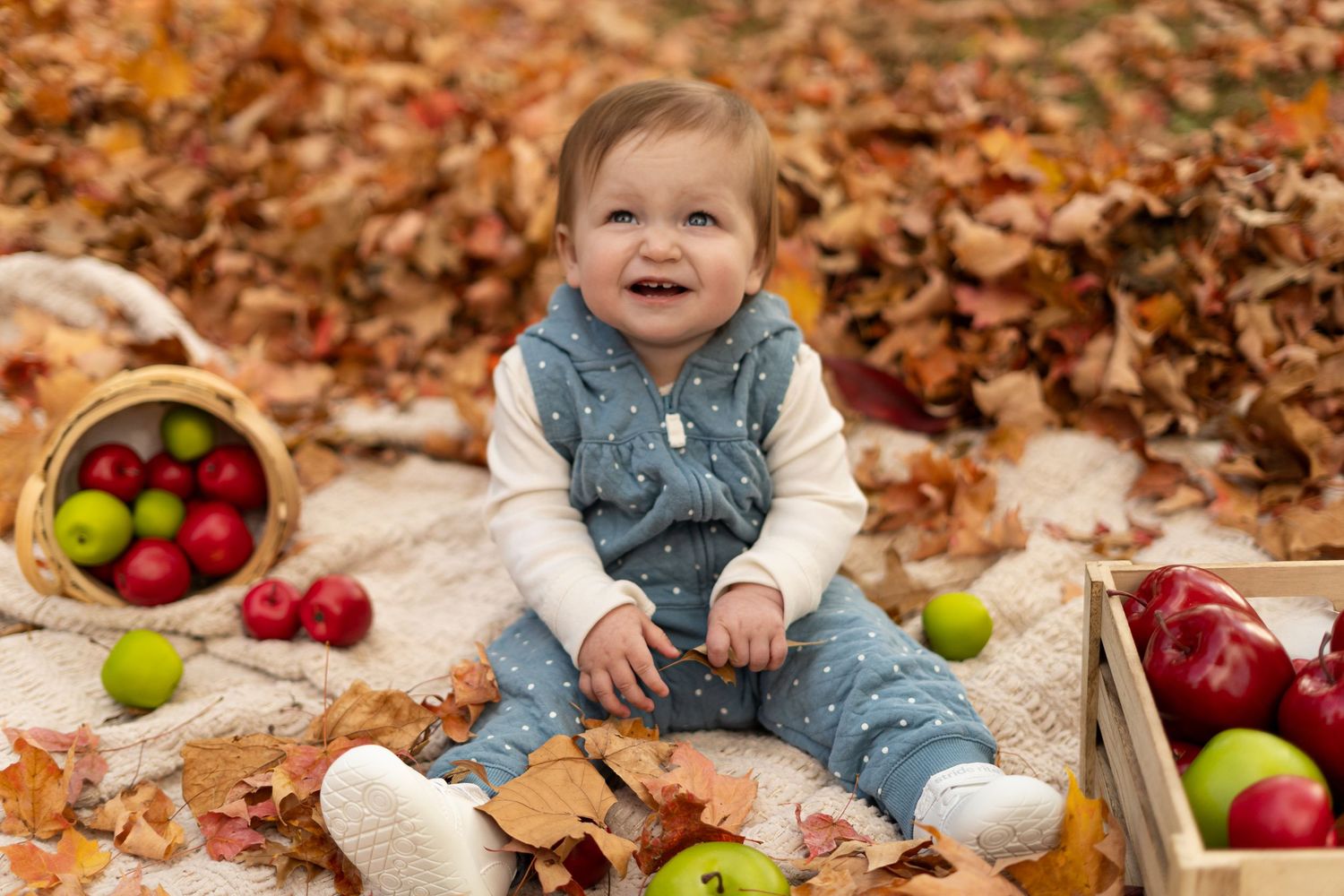 Autumn photoshoot setup with apples and blankets on fallen leaves in a park setting.