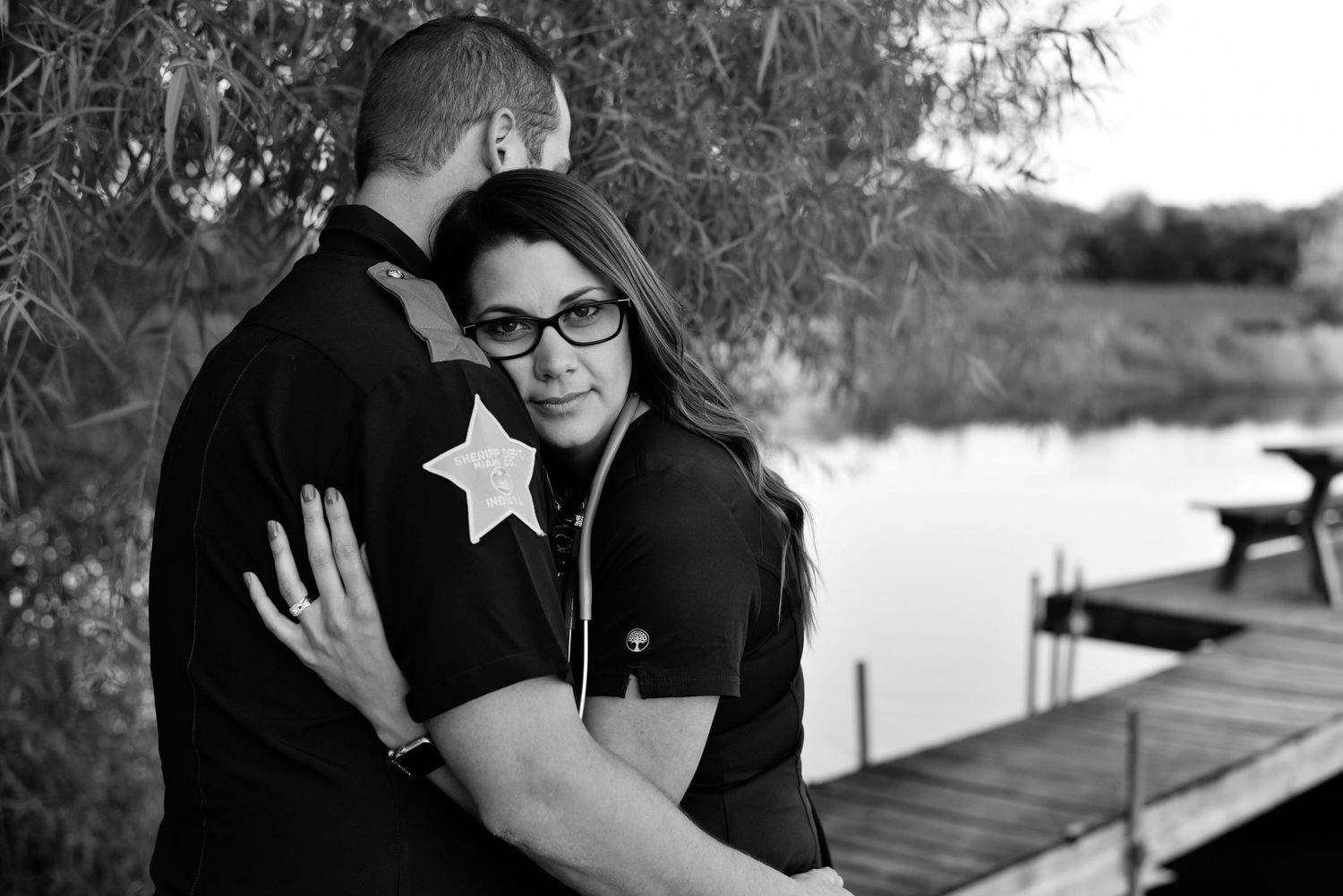 Romantic black and white portrait of a couple embracing by a wooden dock on a peaceful lake.