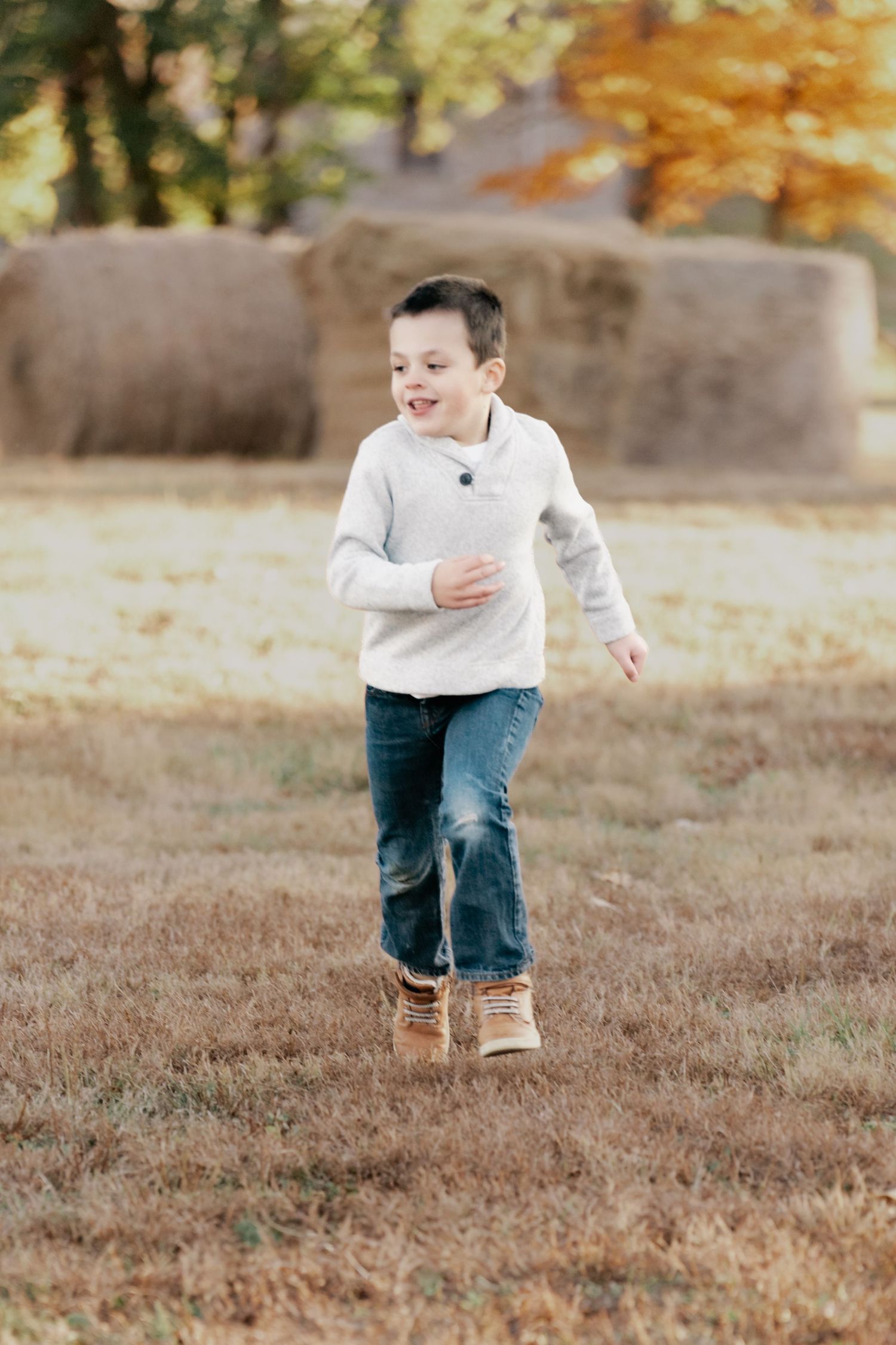 Child running through an autumn field wearing jeans and white sweater.