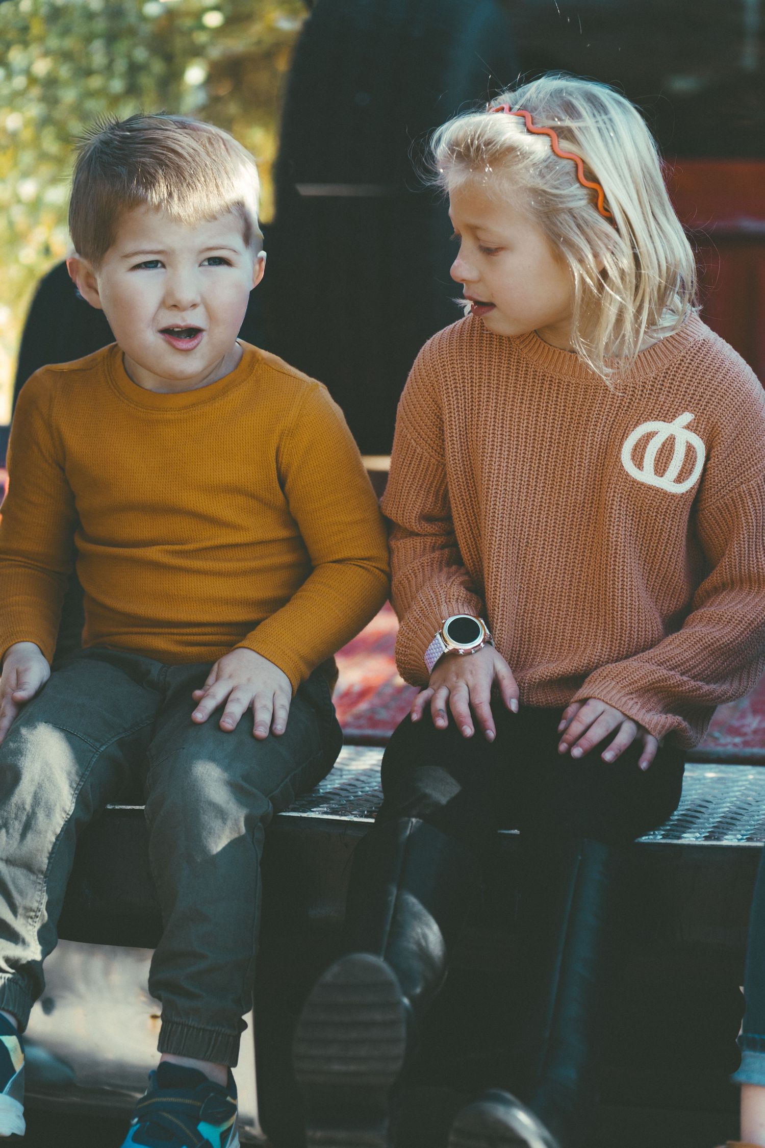 Children sitting together wearing fall-colored sweaters on wooden bench.