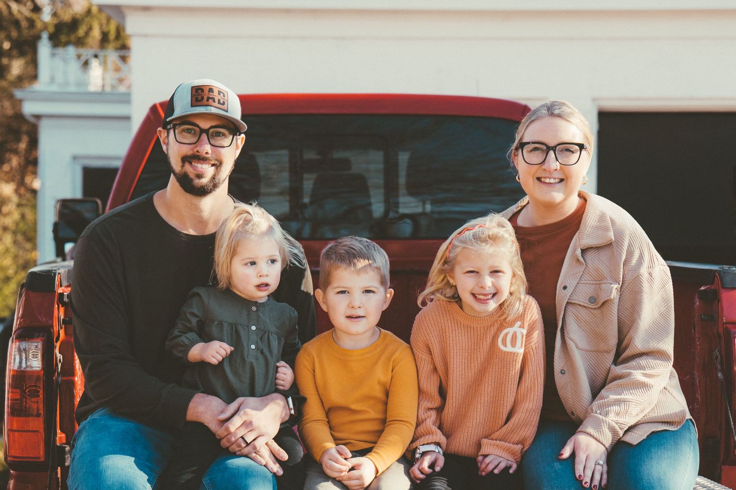 A family of five sitting together on the tailgate of a red pickup truck.