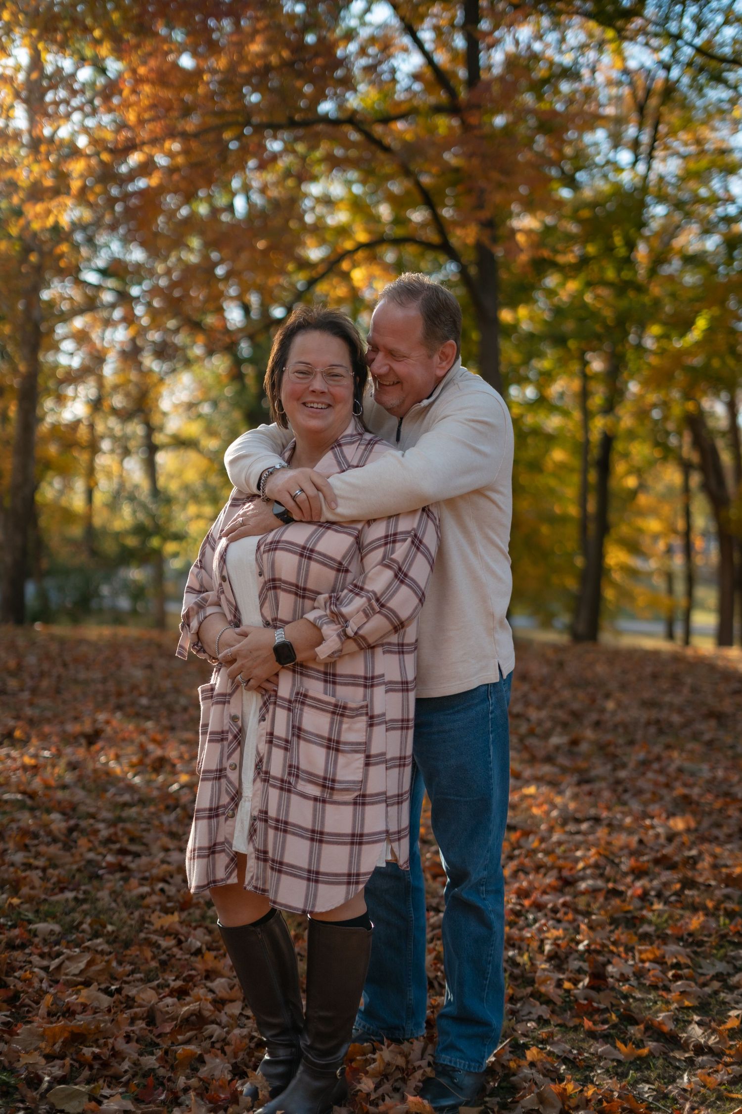 A couple shares a warm hug outdoors during autumn surrounded by fallen leaves.