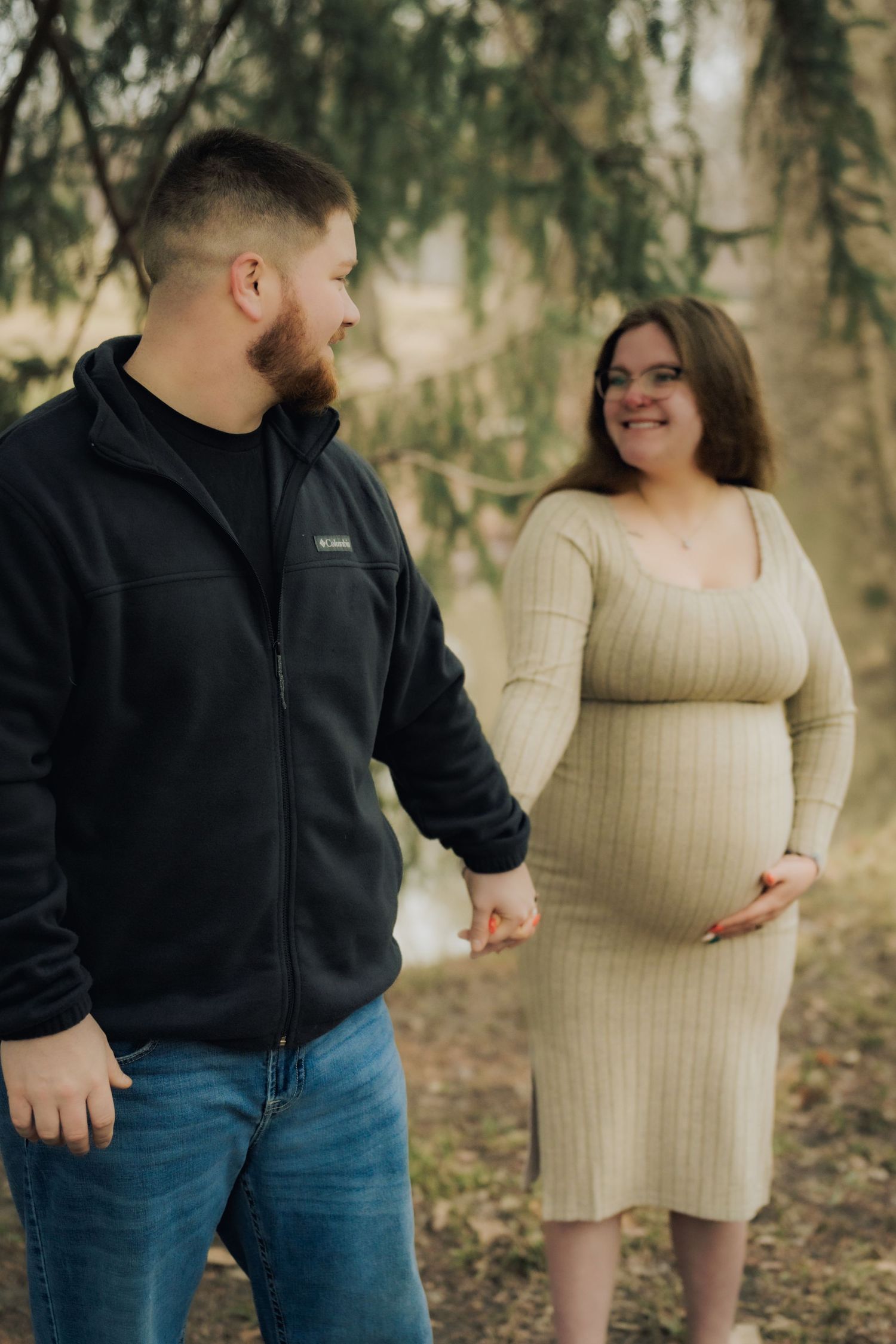 A couple shares a tender moment outdoors as they anticipate their new arrival in a natural woodland setting.
