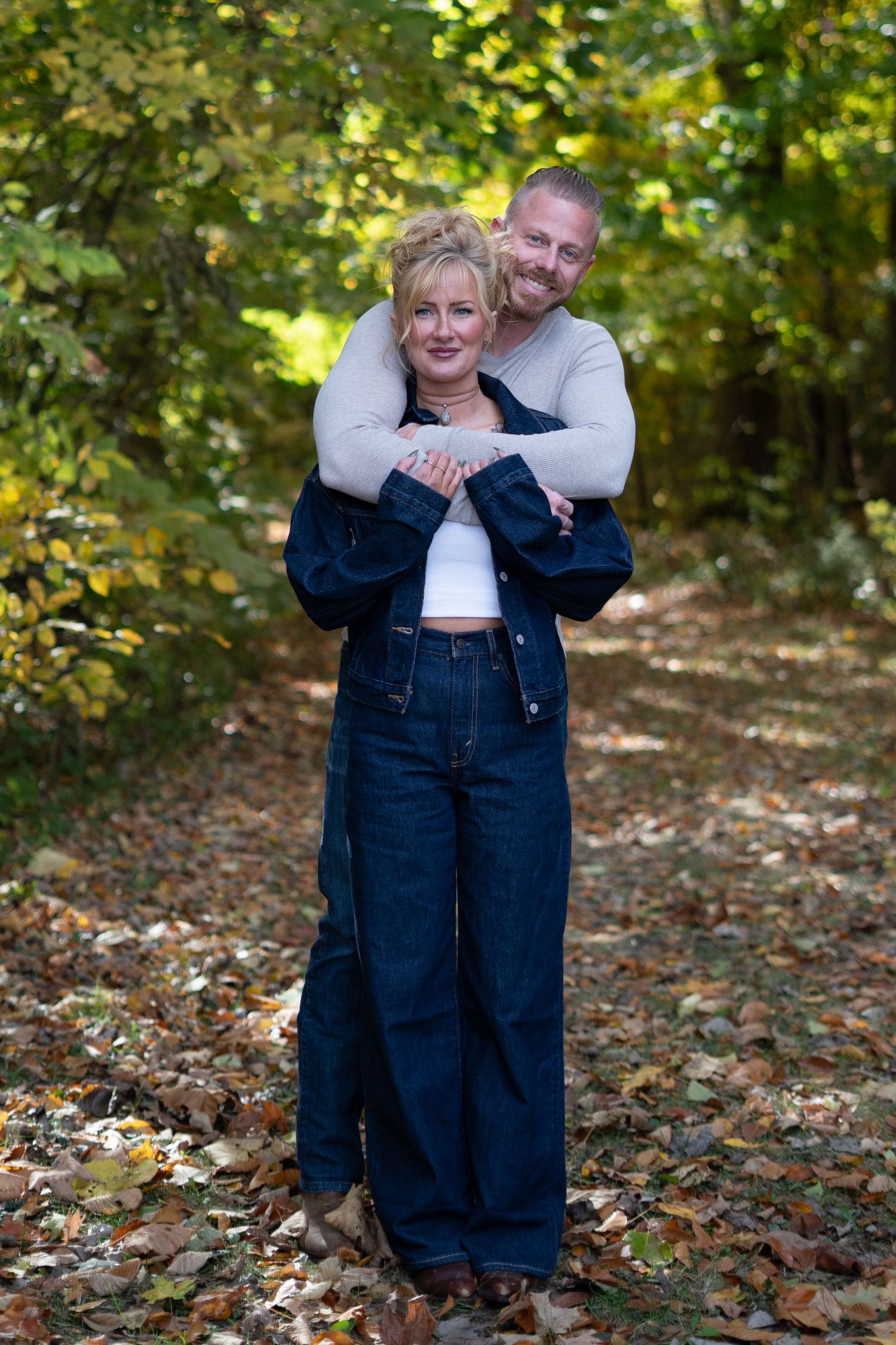 Playful autumn family photoshoot with denim outfits and falling leaves in a wooded setting.
