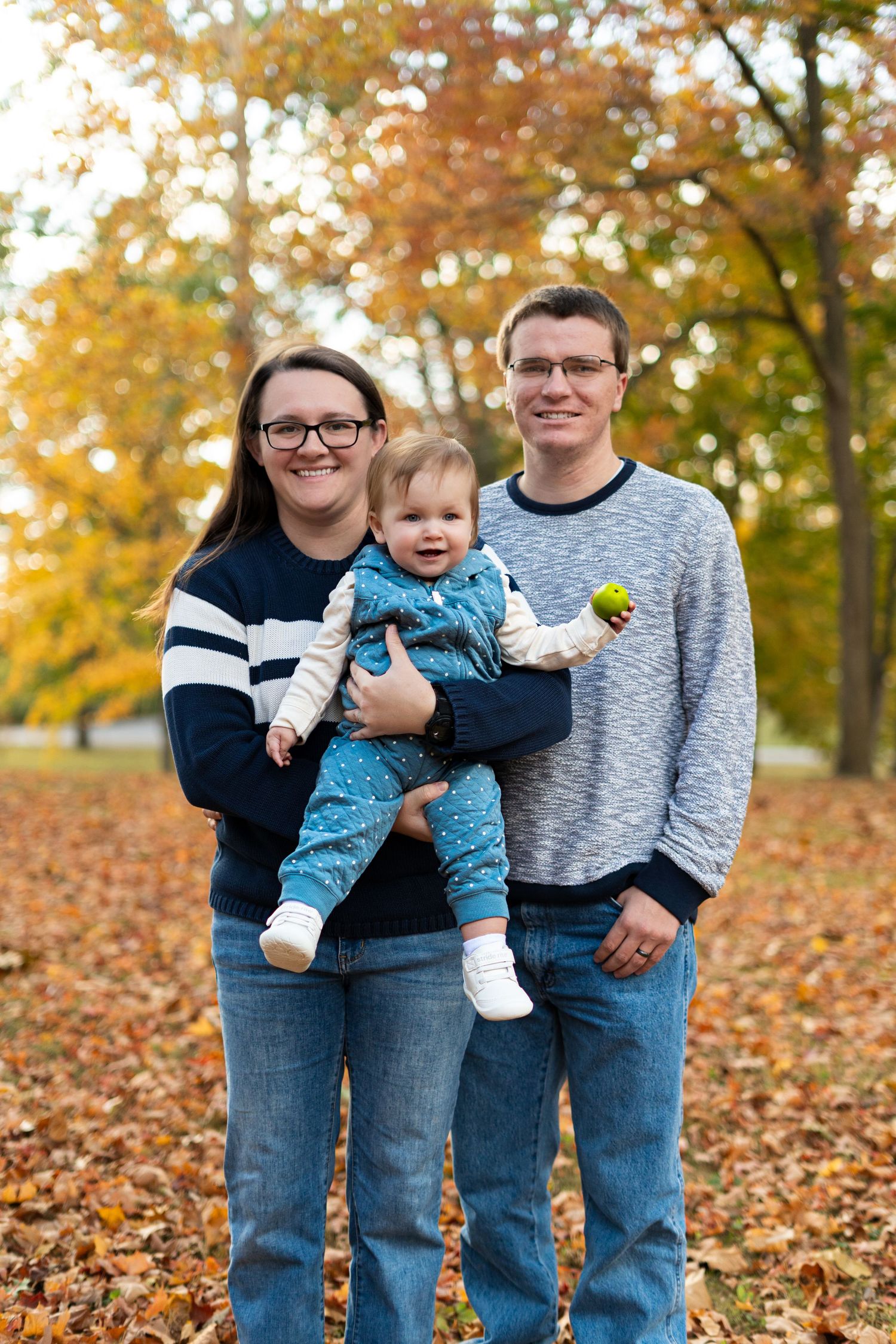 Family of four in coordinating blue and grey outfits posing on fallen autumn leaves.
