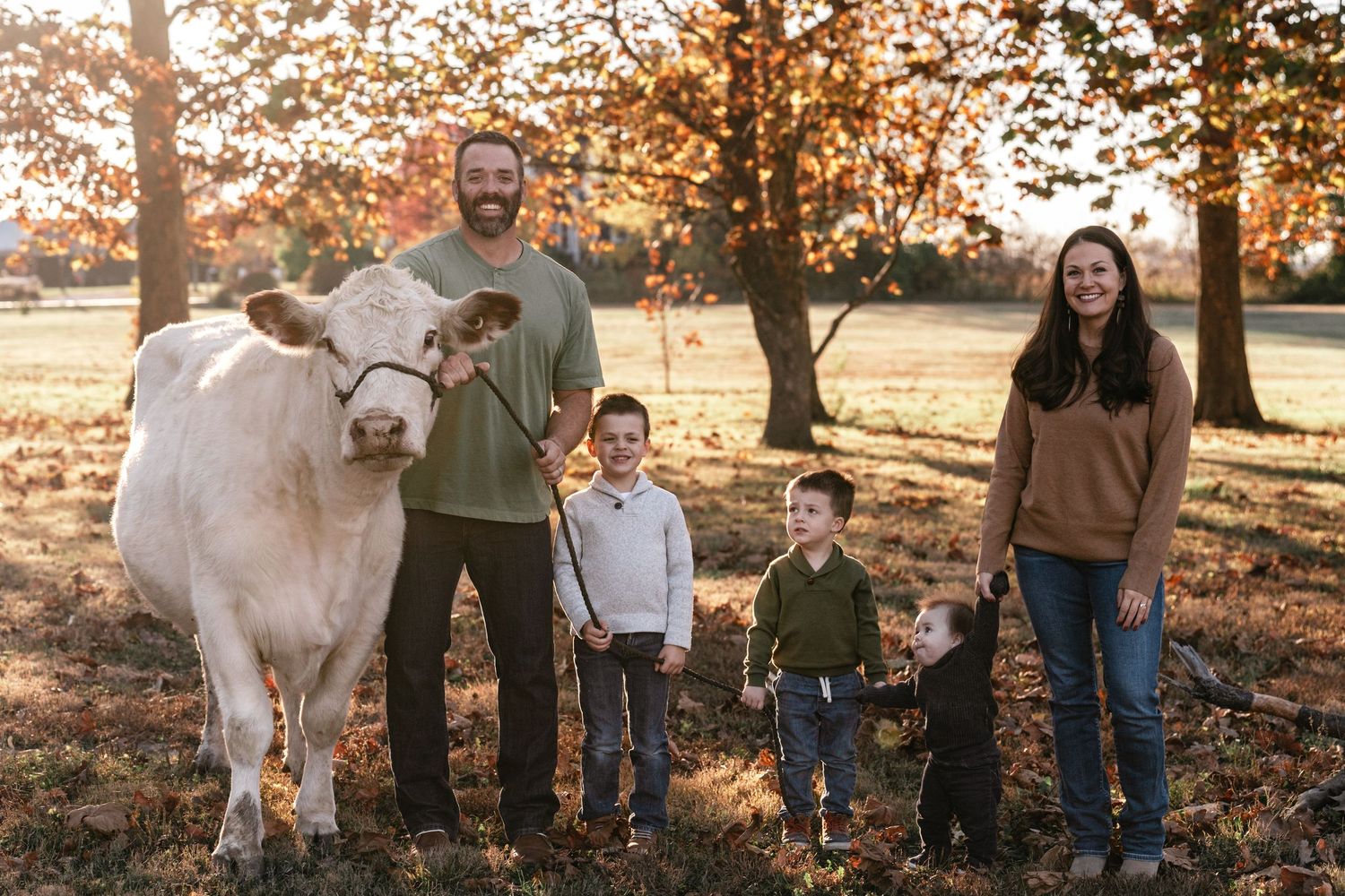 Family and white cow posing together in autumn field with trees.