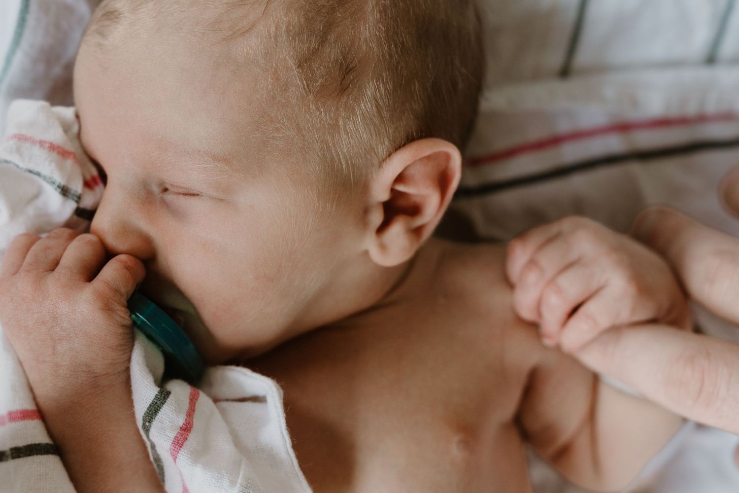 Newborn baby sleeping peacefully with a pacifier, tiny hands visibl during Fresh 48  photo session with Bushel & a Peck Photography