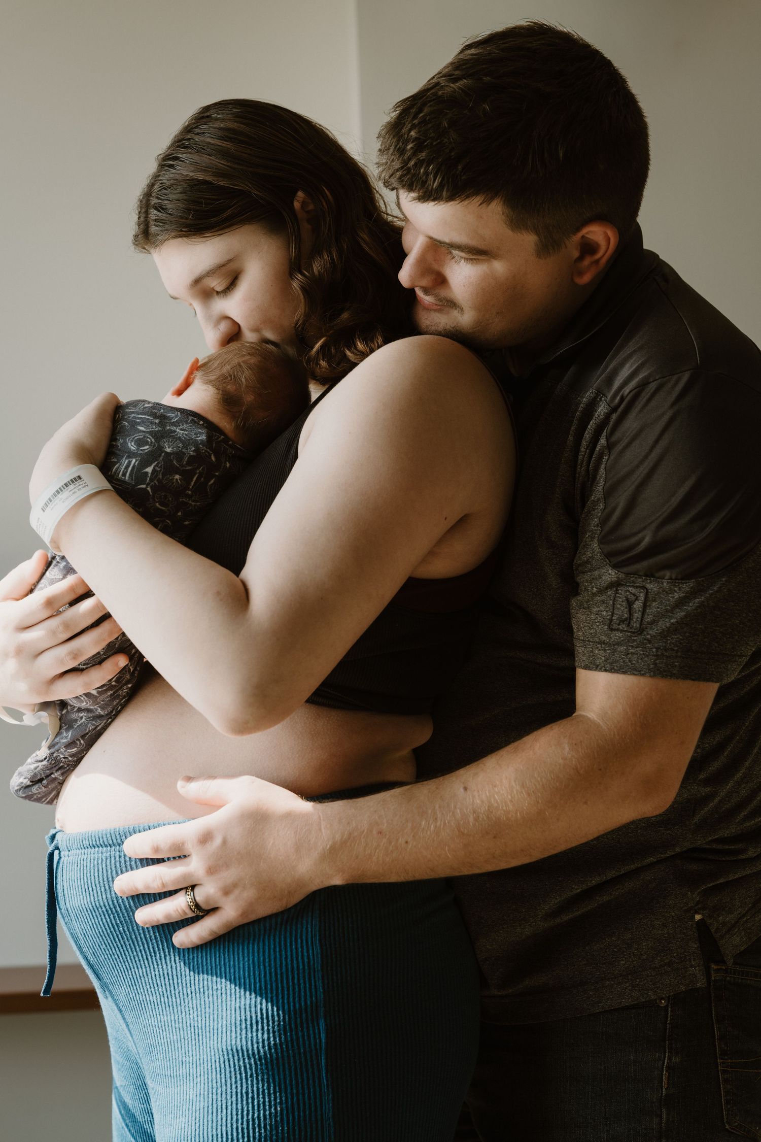 Tender lifestyle newborn portrait of mother kissing her baby while father embraces them both in Miami County Indiana.