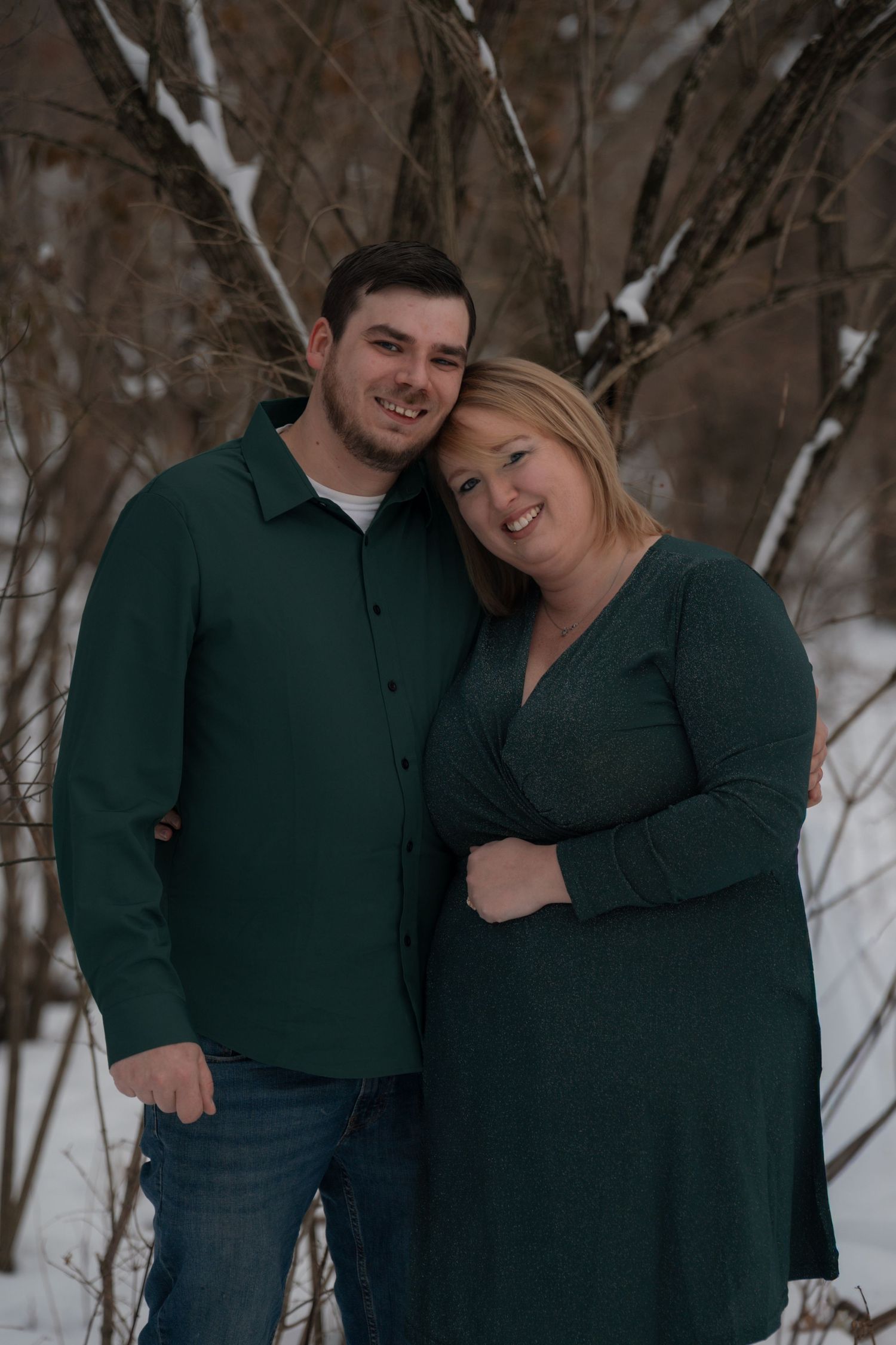Couple embracing in a snowy winter scene wearing matching dark green sweaters.