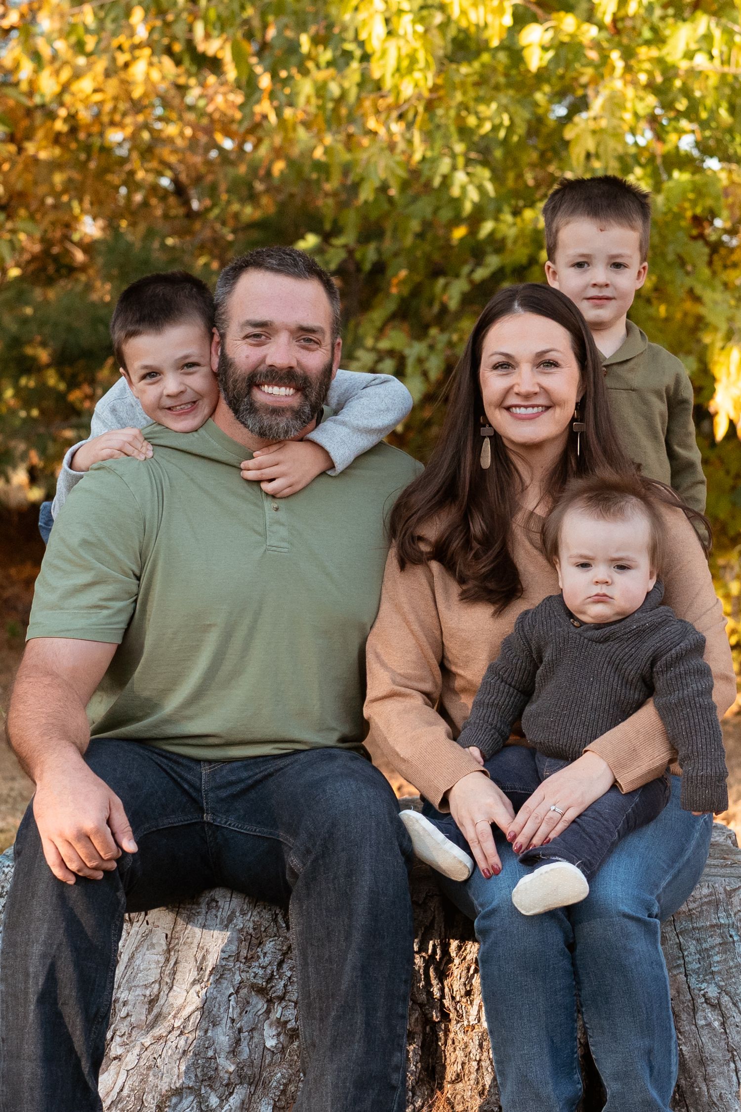 Family sitting together on rustic log bench during autumn photo session.