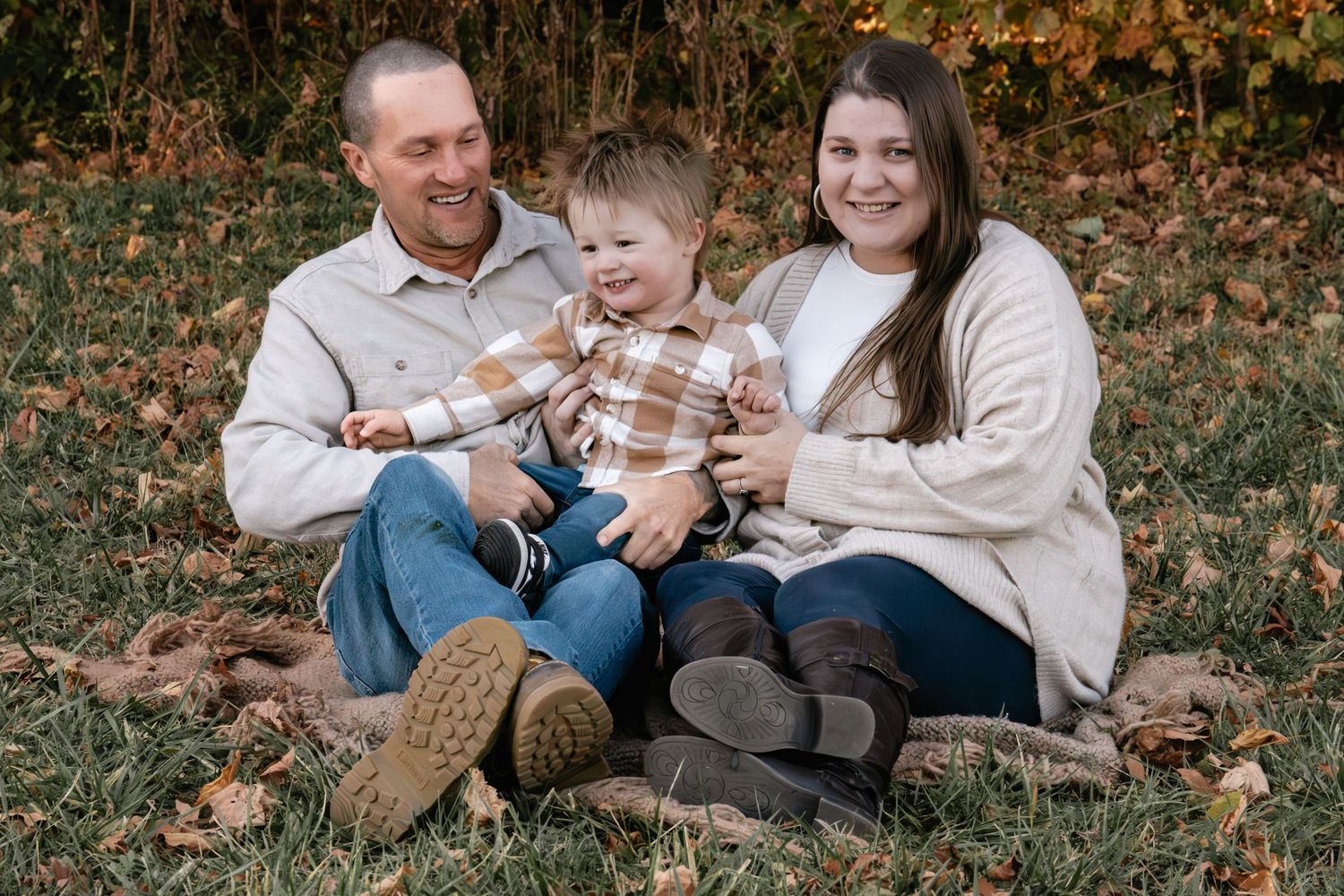 Family shares playful moments while sitting on fallen leaves during autumn photoshoot.