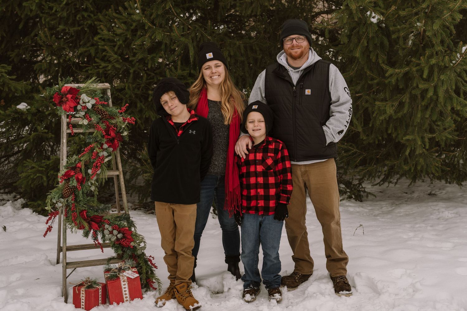 Winter family photo session with red decorations and snow-covered ground.