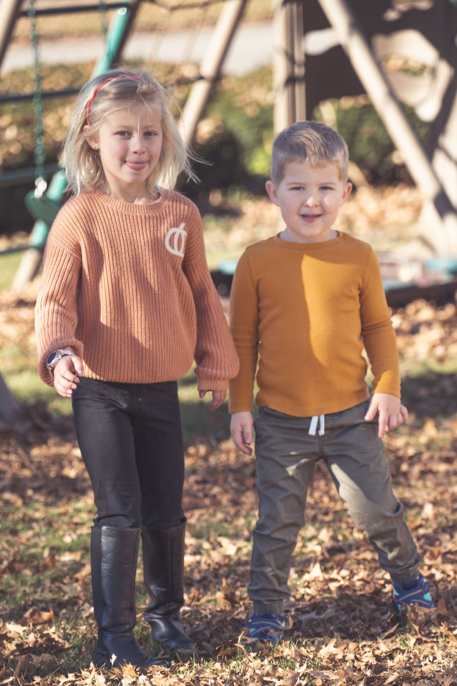 Two children in coordinating sweaters playing in fallen autumn leaves.