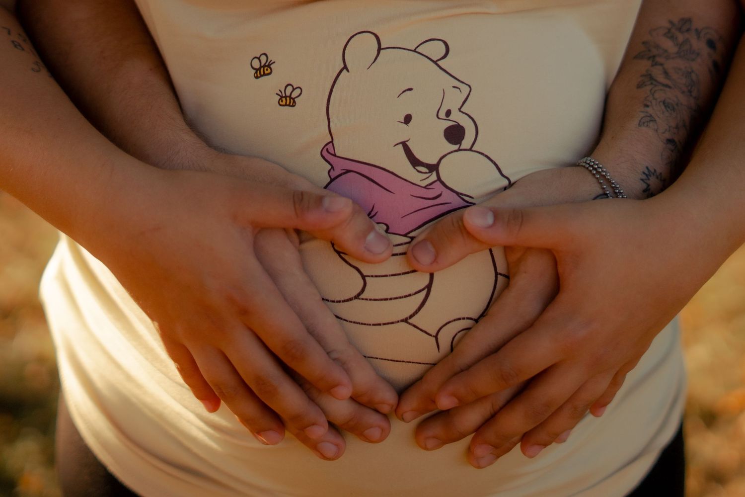 Close-up of hands forming a heart shape over a Winnie the Pooh maternity shirt design.