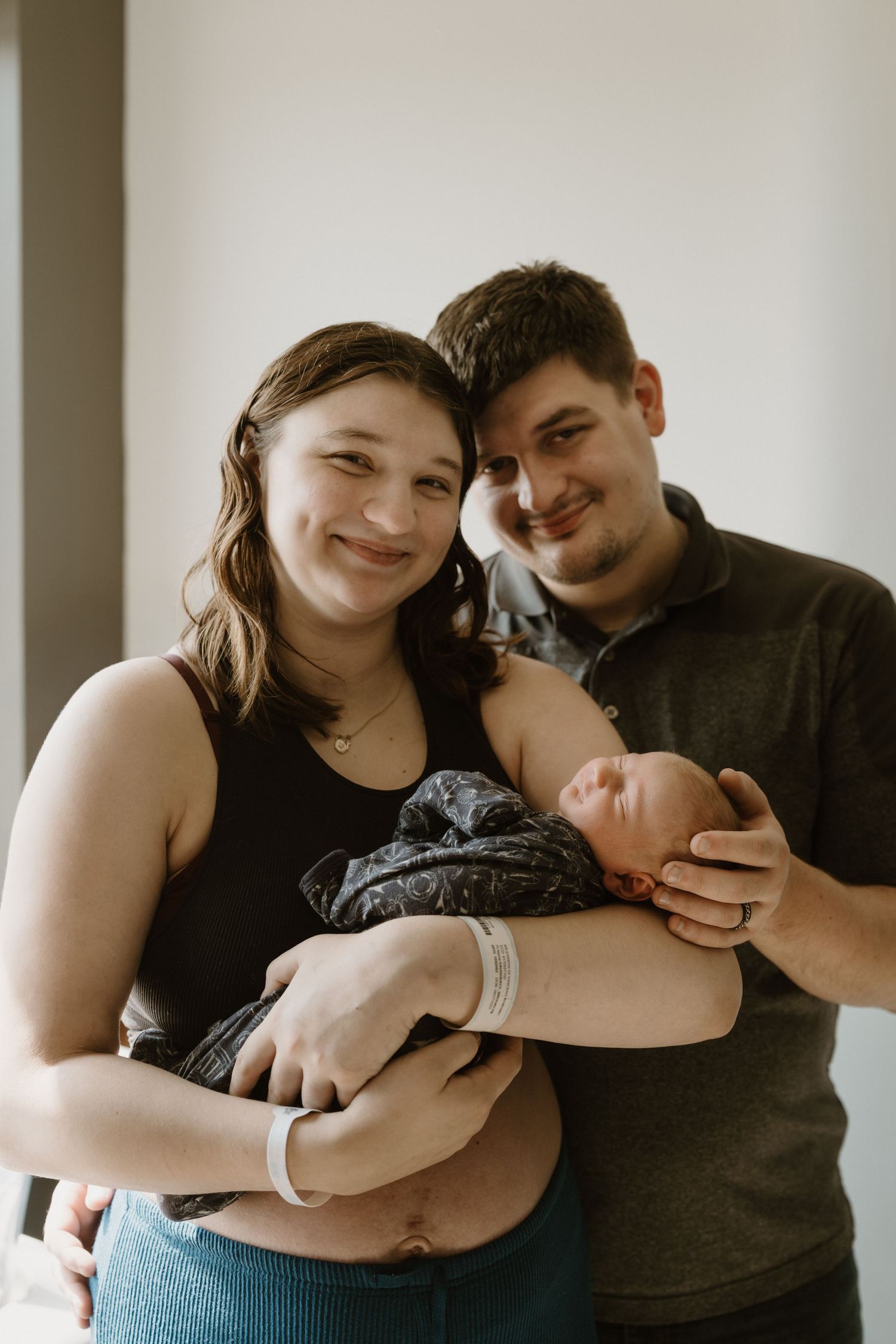 Miami County Indiana newborn photographer capturing a young couple smiling while holding their swaddled baby.