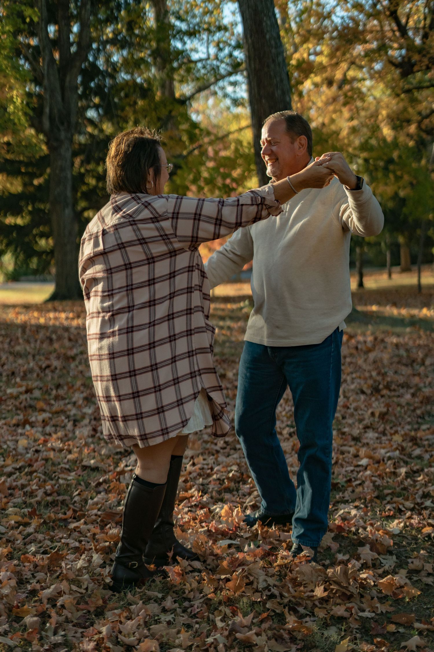A couple dances together on fallen leaves in an autumn park setting.